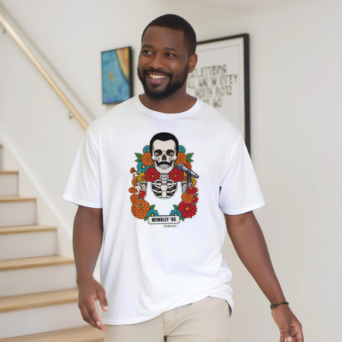 Uomo con la barba sorride vicino a una scala di legno, in casa, e indossa la t-shirt bianca con la calavera Wembley '85