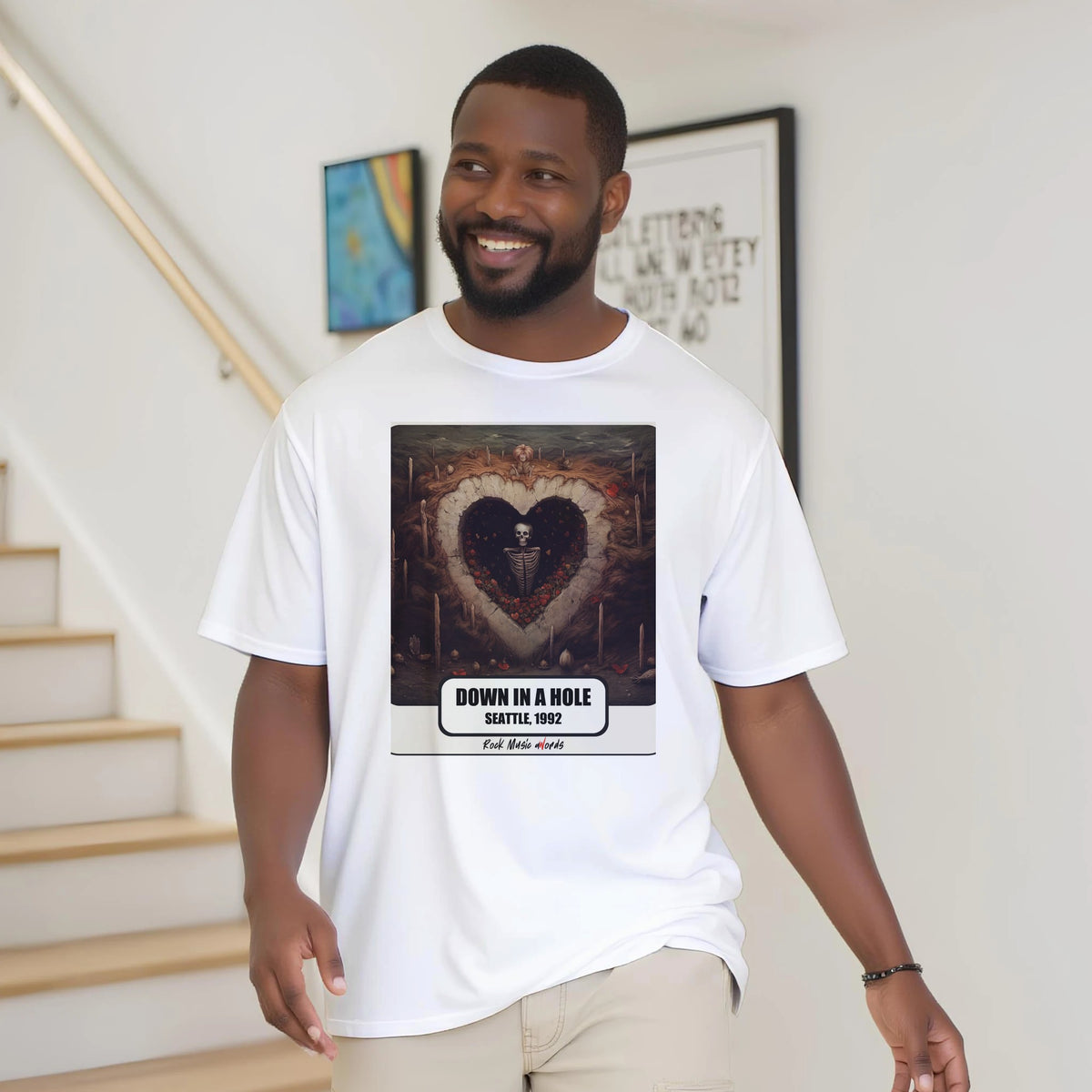 Uomo con la barba sorride vicino a una scala di legno, in casa, e indossa la t-shirt bianca con la stampa Rock Art «Down in a Hole – Seattle, 1992»