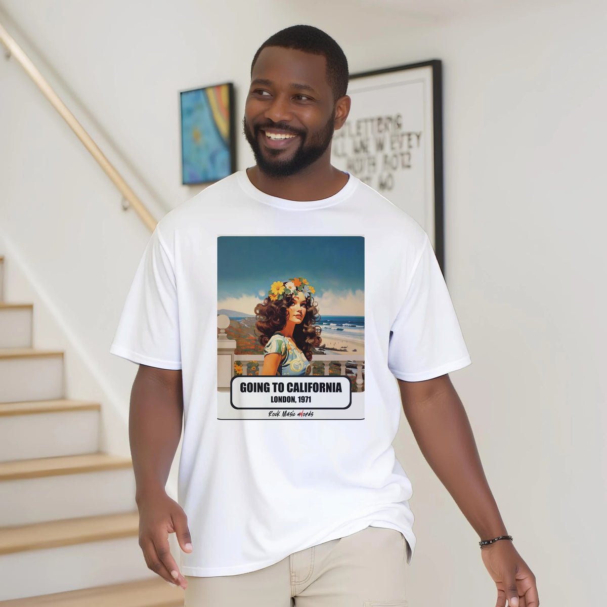 Uomo con la barba sorride vicino a una scala di legno, in casa, e indossa la t-shirt bianca con la stampa Rock Art «Going to California – London, 1971»