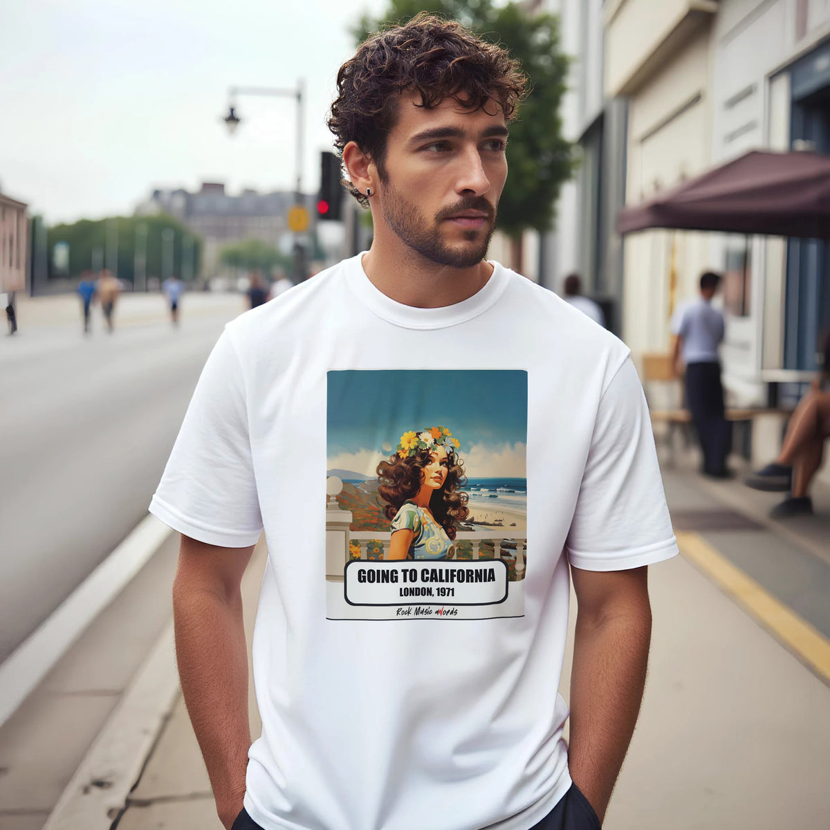 Uomo con capelli ricci e barba su un marciapiede di città indossa la t-shirt bianca con la stampa Rock Art «Going to California – London, 1971»