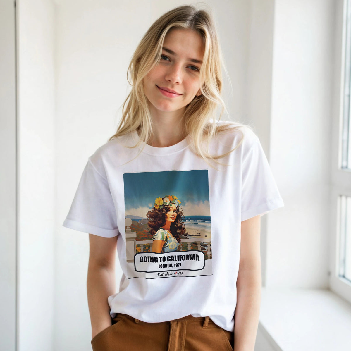 Ragazza bionda con le mani in tasca, accanto a una finestra, indossa la t-shirt bianca con la stampa Rock Art «Going to California – London, 1971»