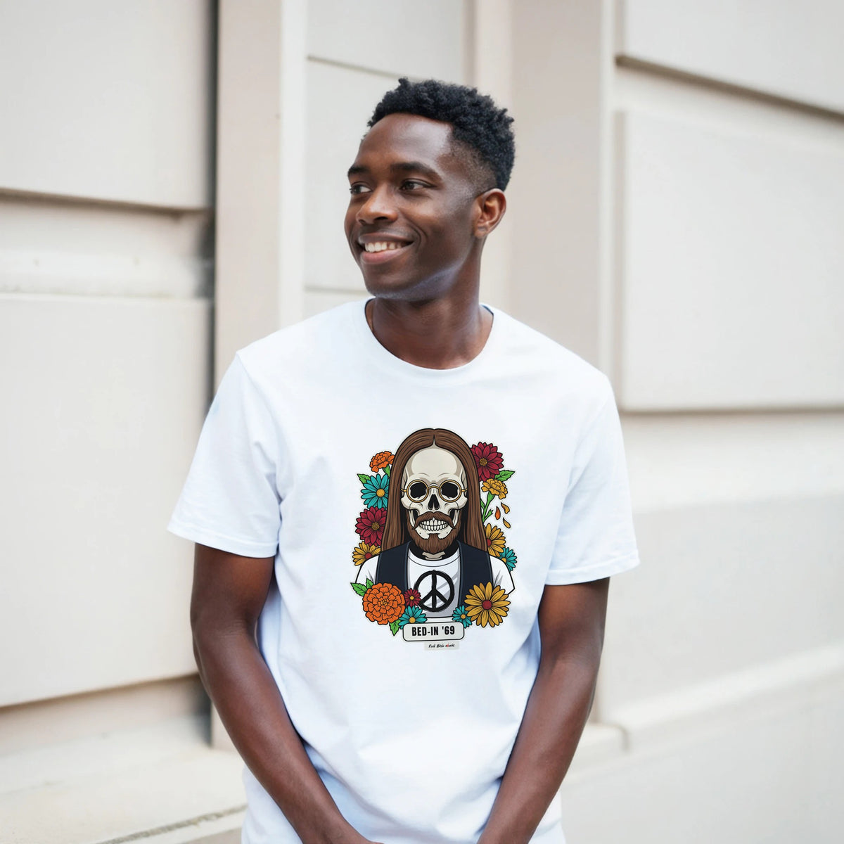 Ragazzo sorridente davanti a un muro chiaro a blocchi indossa la t-shirt bianca con la calavera Bed-In '69