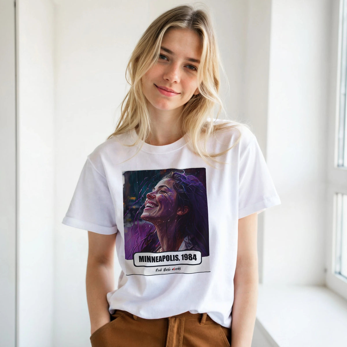 Ragazza bionda con le mani in tasca, accanto a una finestra, indossa la t-shirt bianca con la stampa Rock Art «Purple Rain – Minneapolis, 1984»