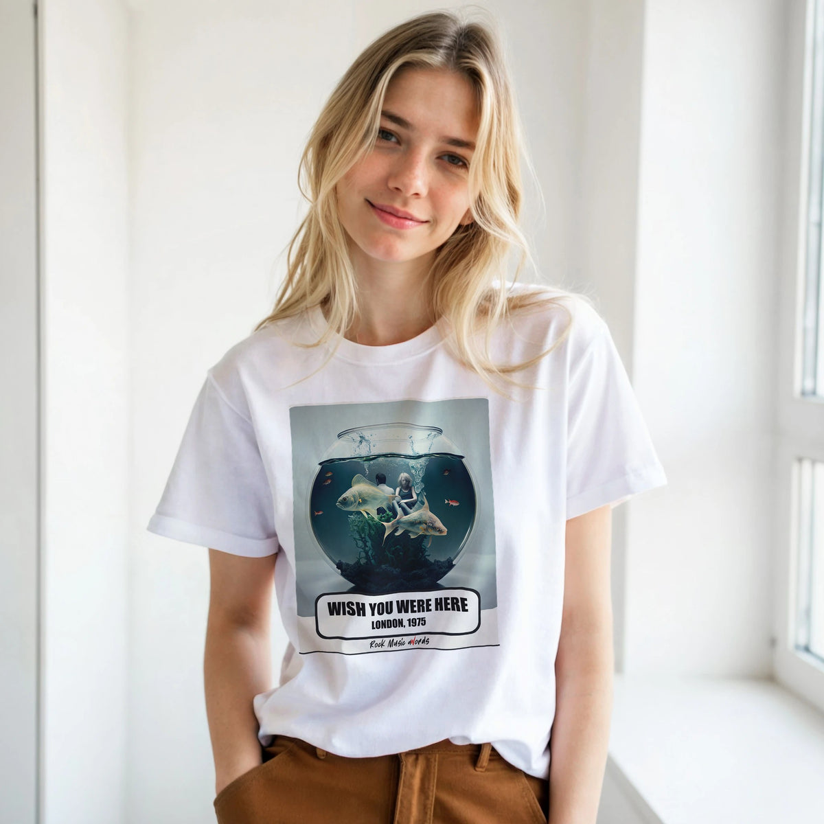 Ragazza bionda con le mani in tasca, accanto a una finestra, indossa la t-shirt bianca con la stampa Rock Art «Wish You Were Here – London, 1975»