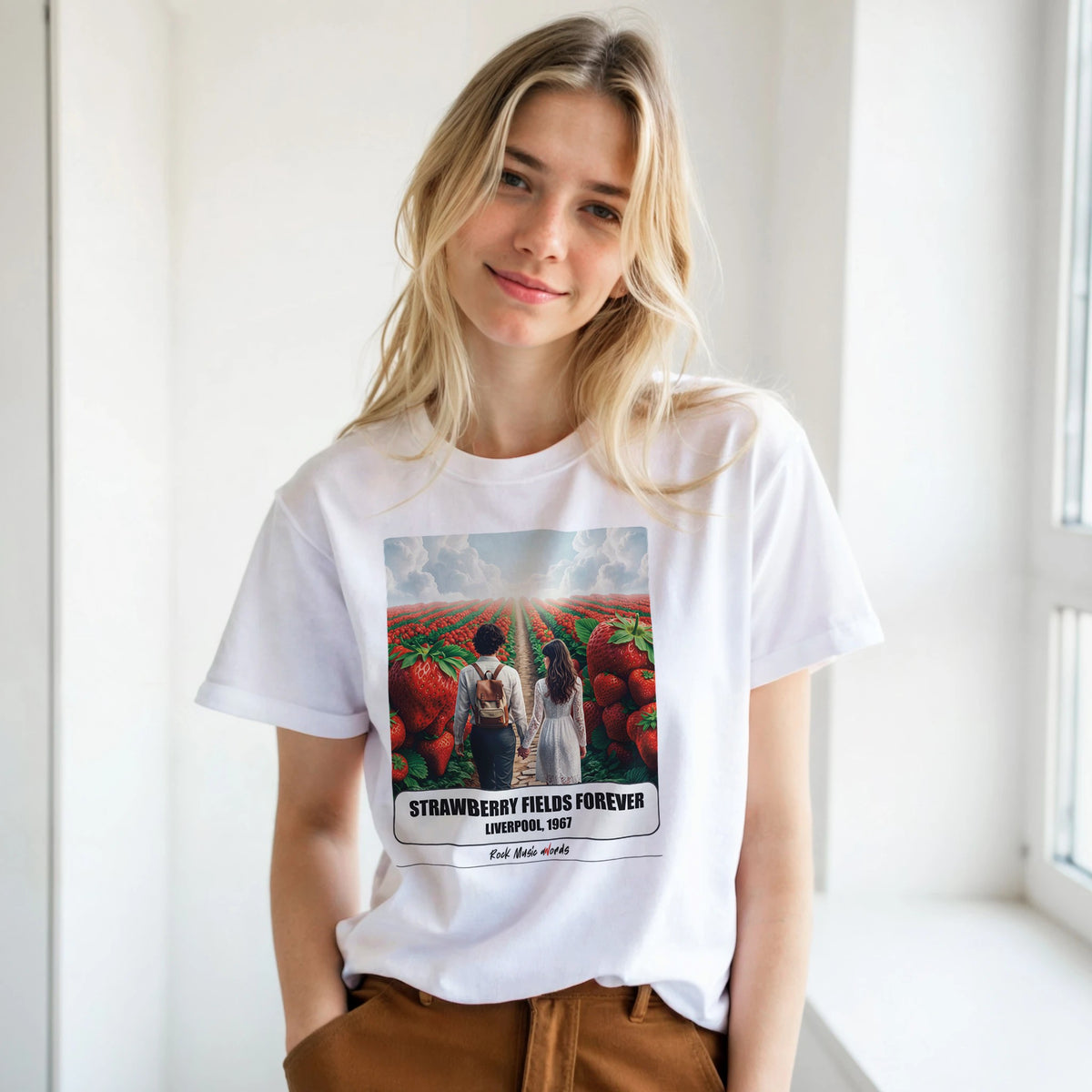 Ragazza bionda con le mani in tasca, accanto a una finestra, indossa la t-shirt bianca con la stampa Rock Art «Strawberry Fields Forever – Liverpool, 1967»
