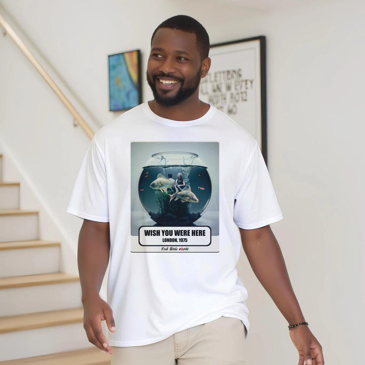 Uomo con la barba sorride vicino a una scala di legno, in casa, e indossa la t-shirt bianca con la stampa Rock Art «Wish You Were Here – London, 1975»