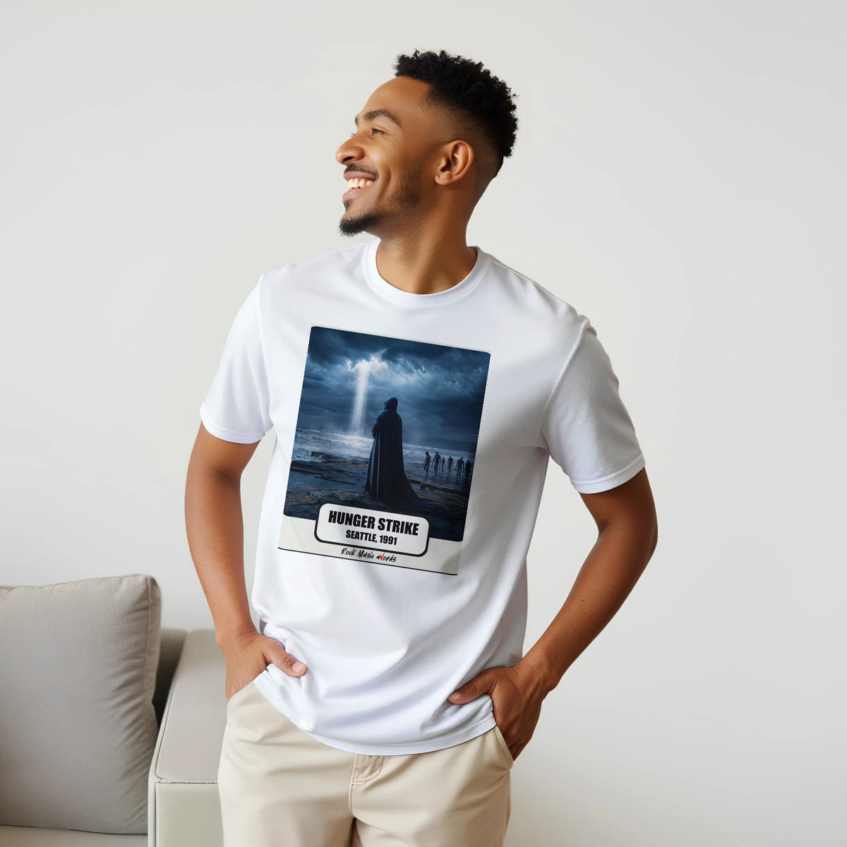 Uomo sorridente con le mani sui fianchi, accanto a un divano, indossa la t-shirt bianca con la stampa Rock Art «Hunger Strike – Seattle, 1991»