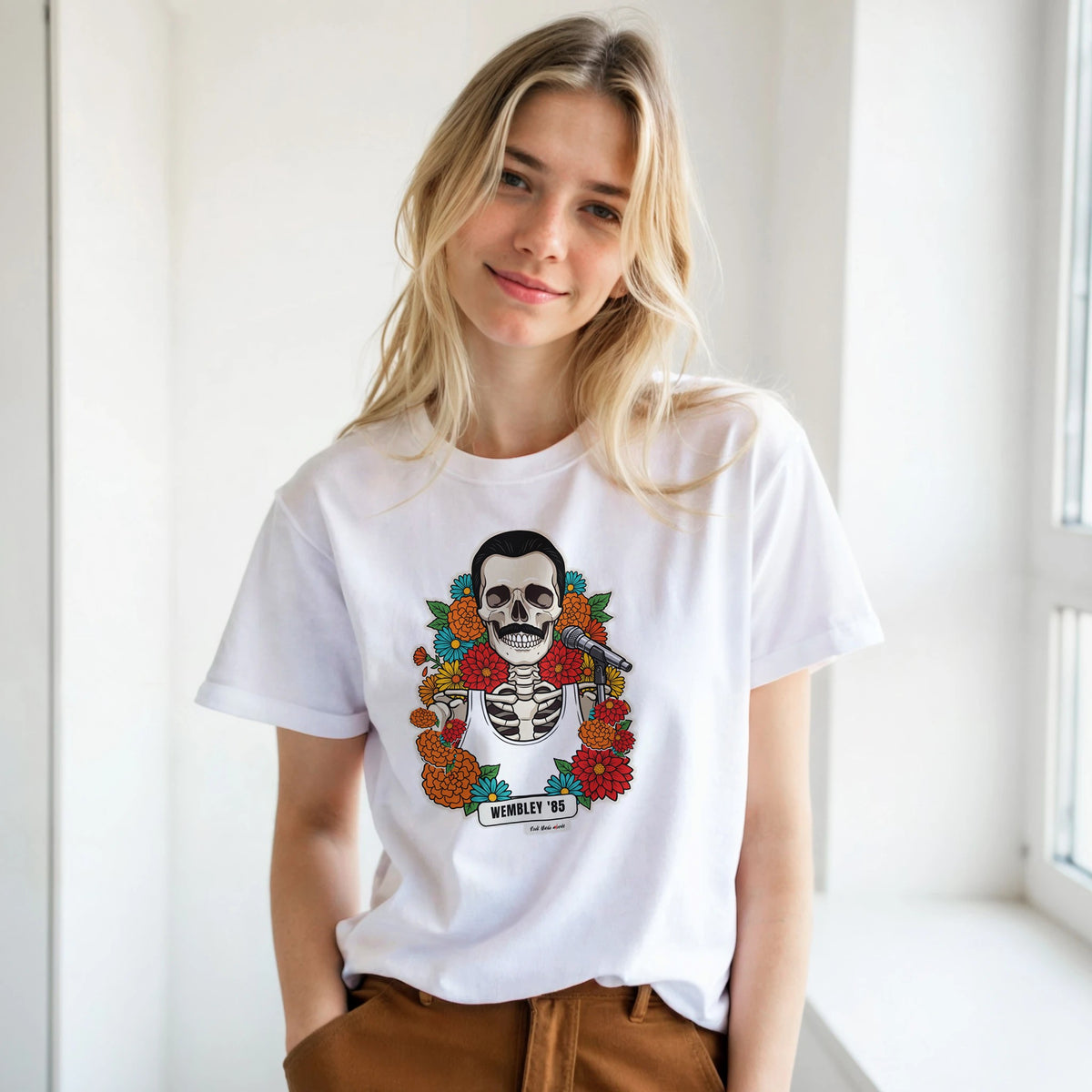 Ragazza bionda con le mani in tasca, accanto a una finestra, indossa la t-shirt bianca con la calavera Wembley '85