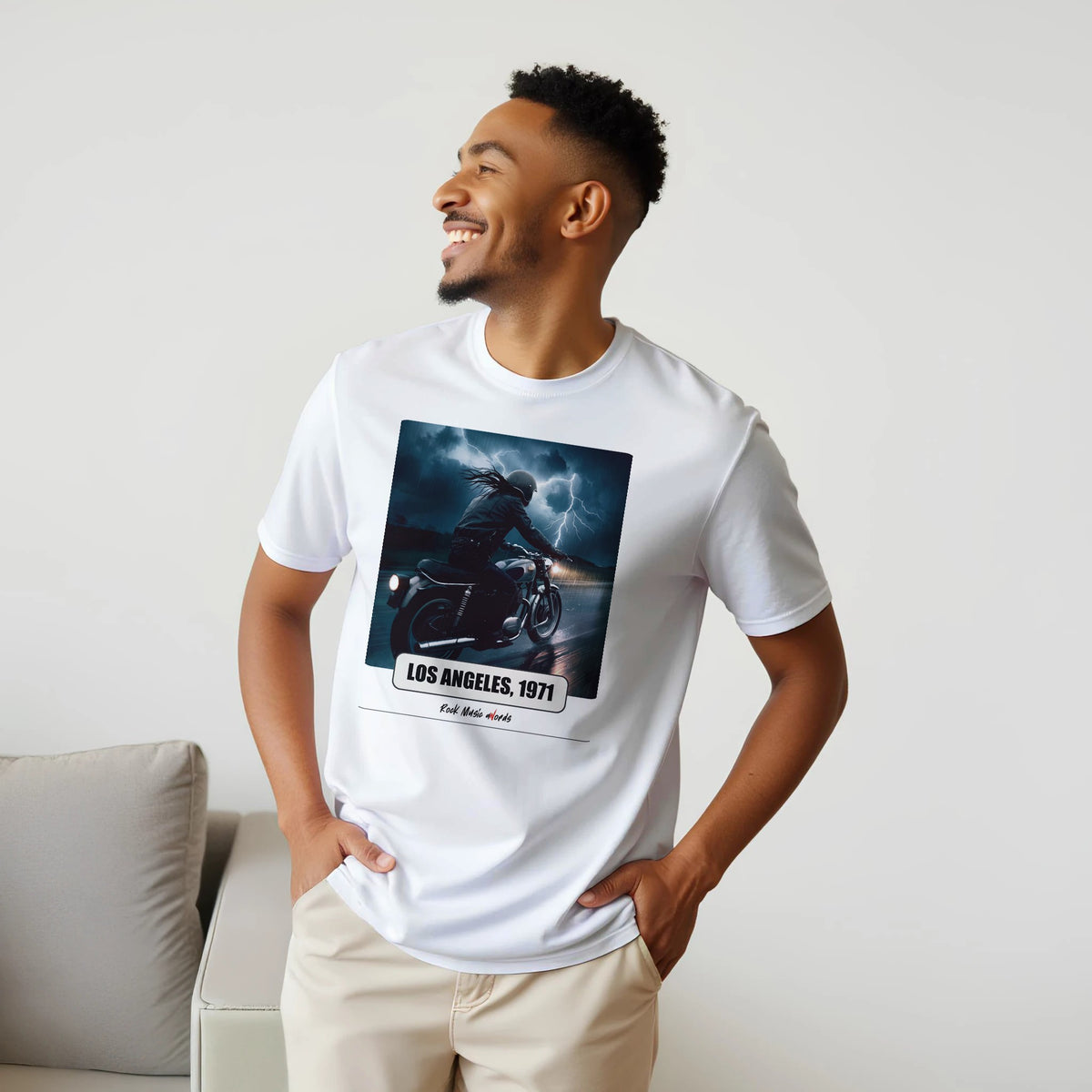 Uomo sorridente con le mani sui fianchi, accanto a un divano, indossa la t-shirt bianca con la stampa Rock Art «Riders on the Storm – Los Angeles, 1971»