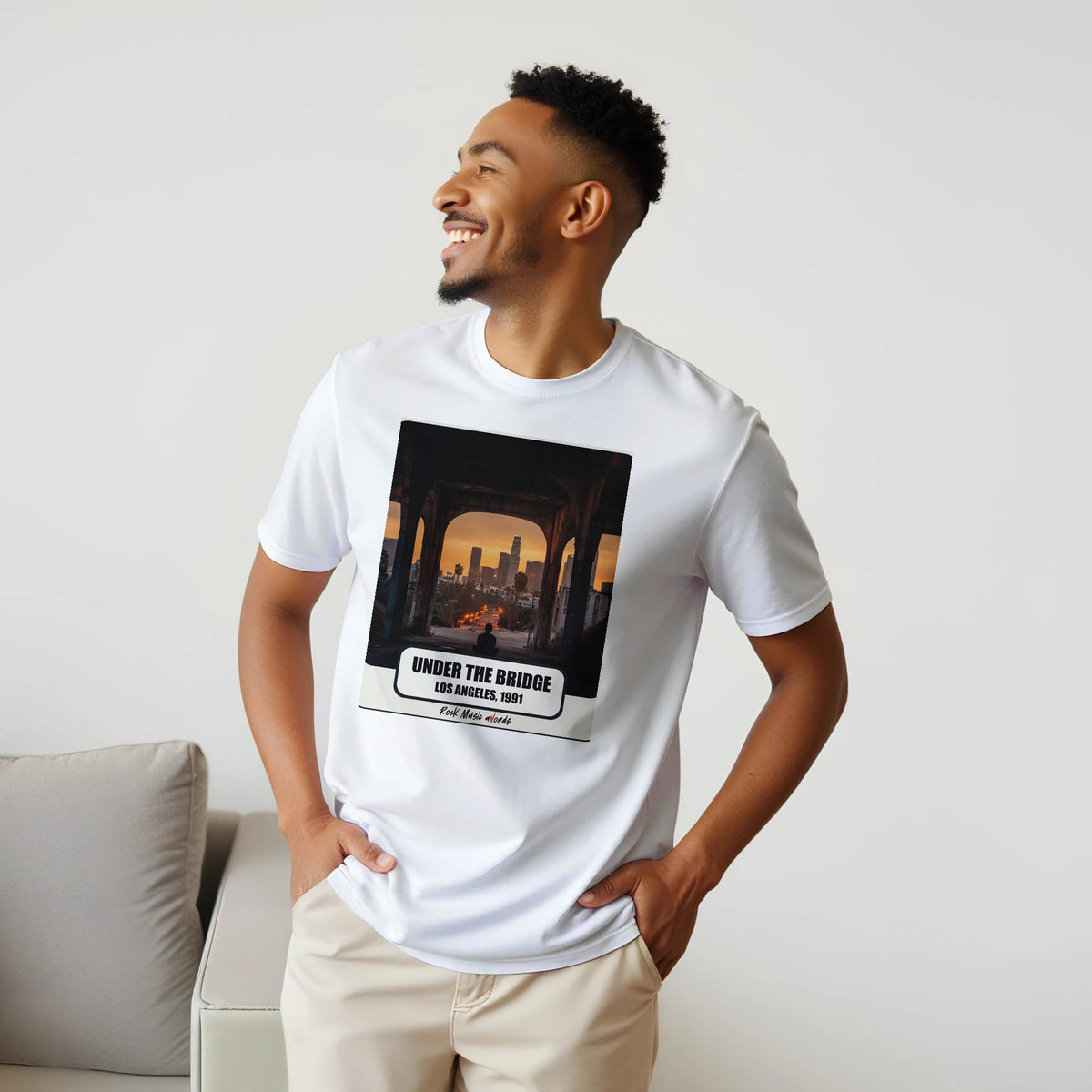 Uomo sorridente con le mani sui fianchi, accanto a un divano, indossa la t-shirt bianca con la stampa Rock Art «Under the Bridge – Los Angeles, 1991»