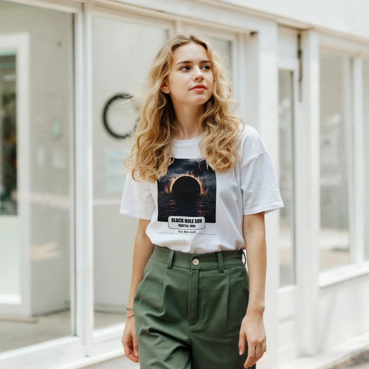 Ragazza bionda davanti a una facciata a vetrate indossa la t-shirt bianca con la stampa Rock Art «Black Hole Sun – Seattle, 1994» e pantaloni verdi