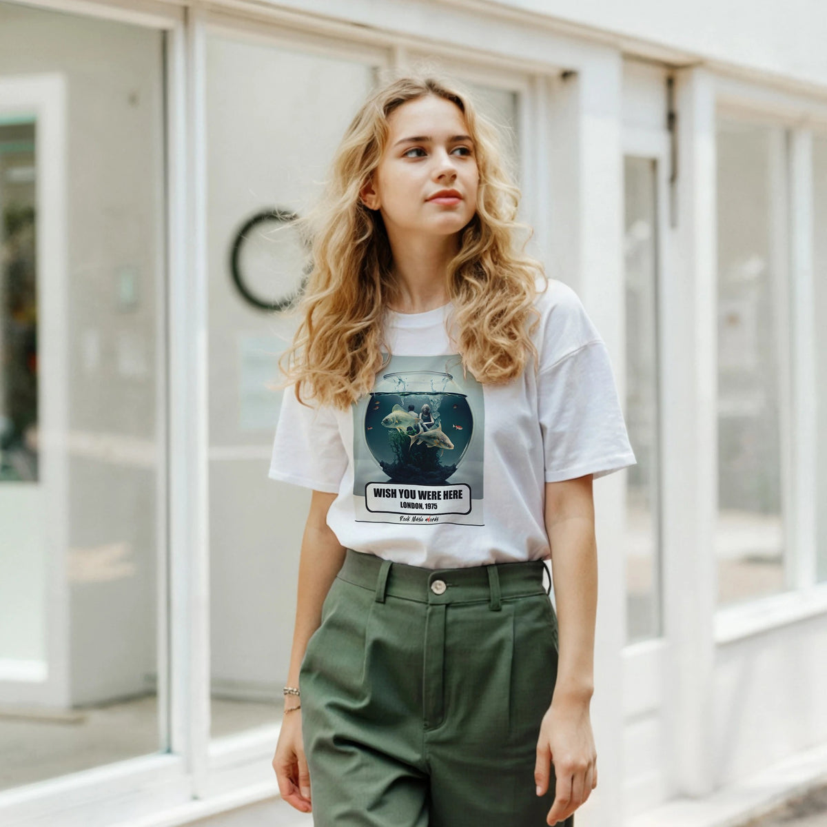 Ragazza bionda davanti a una facciata a vetrate indossa la t-shirt bianca con la stampa Rock Art «Wish You Were Here – London, 1975» e pantaloni verdi
