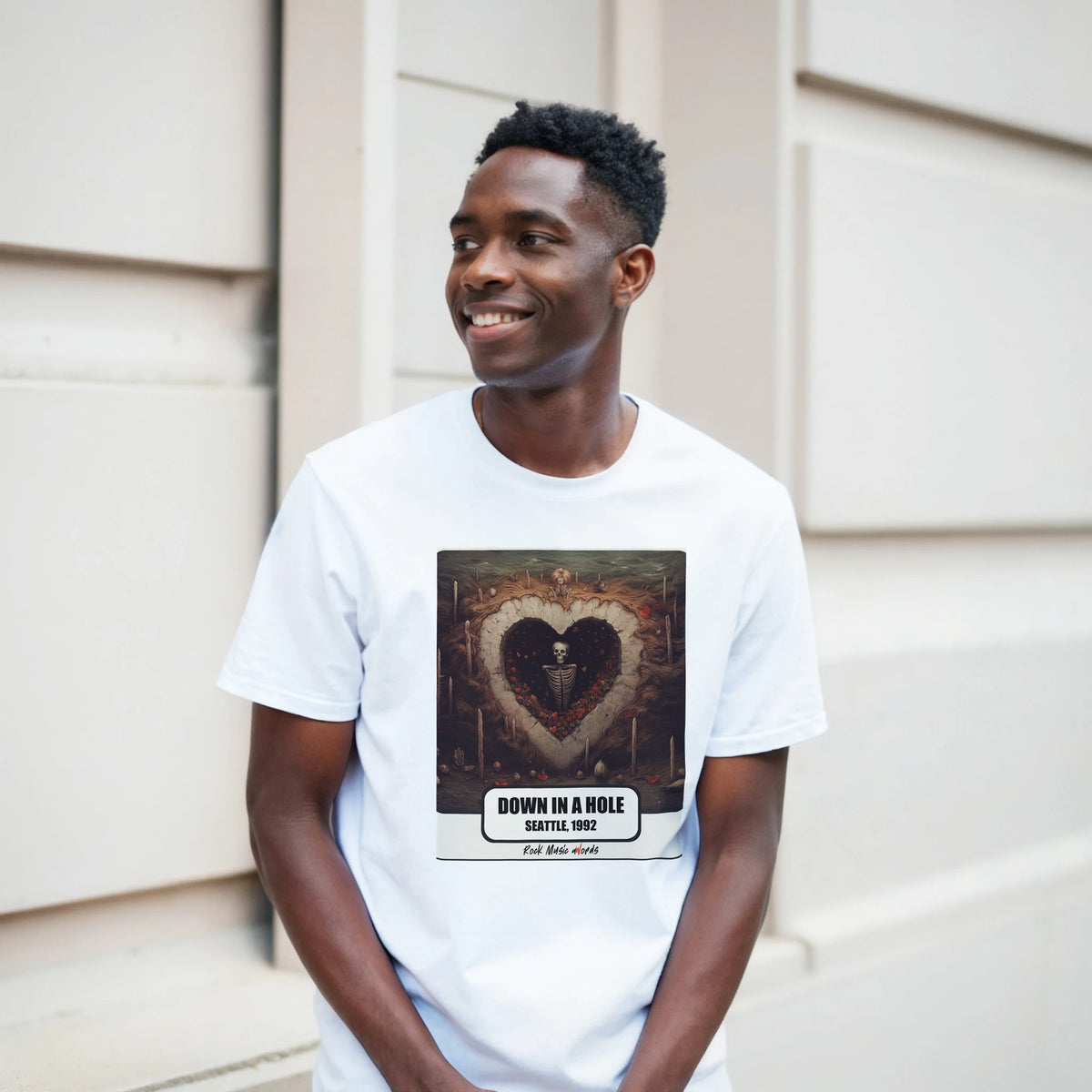 Ragazzo sorridente davanti a un muro chiaro a blocchi indossa la t-shirt bianca con la stampa Rock Art «Down in a Hole – Seattle, 1992»