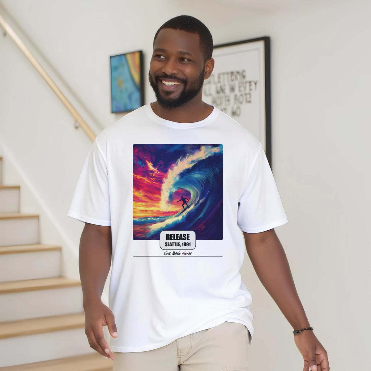 Uomo con la barba sorride vicino a una scala di legno, in casa, e indossa la t-shirt bianca con la stampa Rock Art «Release – Seattle, 1991»
