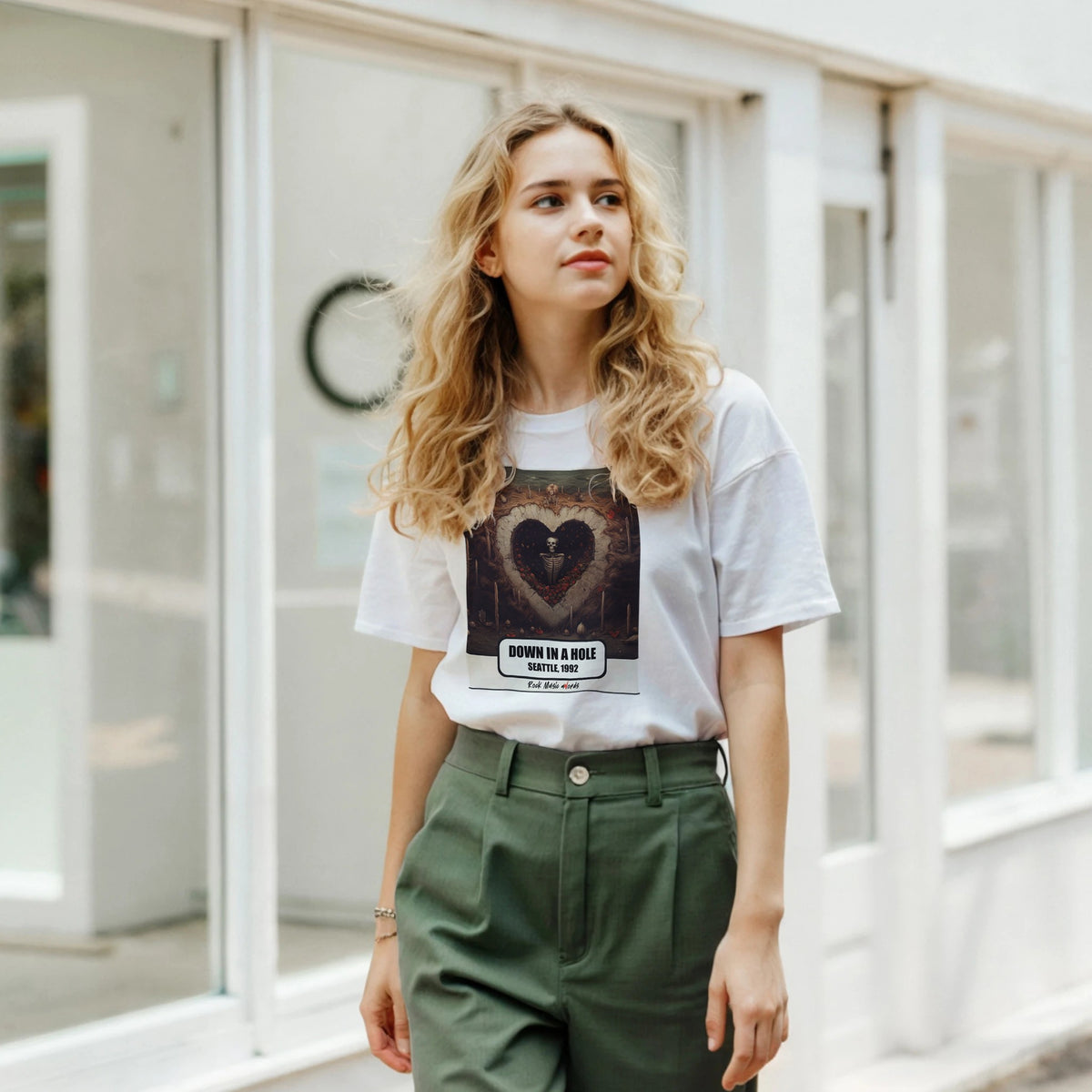 Ragazza bionda davanti a una facciata a vetrate indossa la t-shirt bianca con la stampa Rock Art «Down in a Hole – Seattle, 1992» e pantaloni verdi