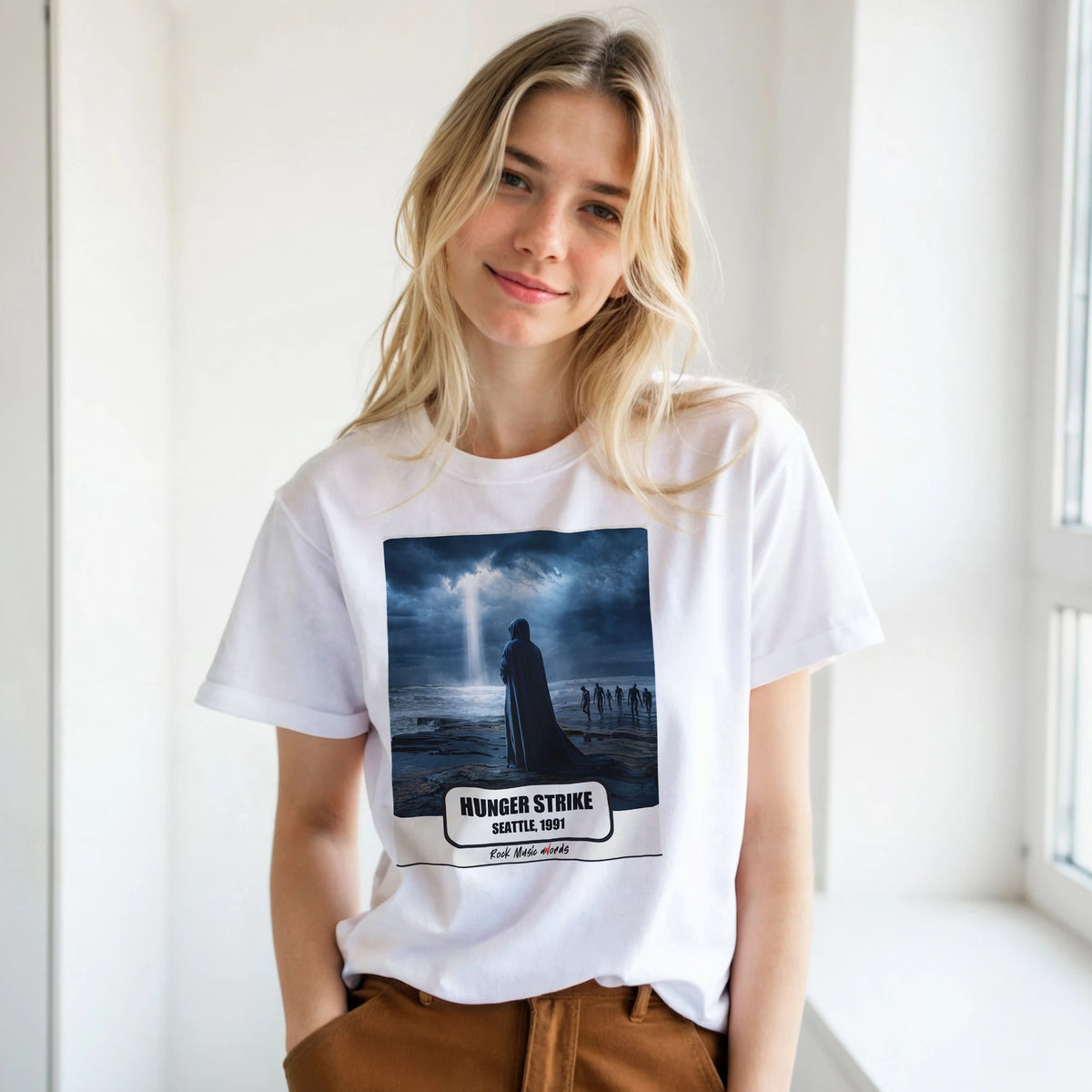 Ragazza bionda con le mani in tasca, accanto a una finestra, indossa la t-shirt bianca con la stampa Rock Art «Hunger Strike – Seattle, 1991»