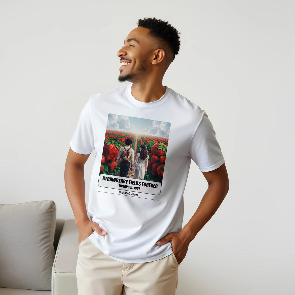 Uomo sorridente con le mani sui fianchi, accanto a un divano, indossa la t-shirt bianca con la stampa Rock Art «Strawberry Fields Forever – Liverpool, 1967»