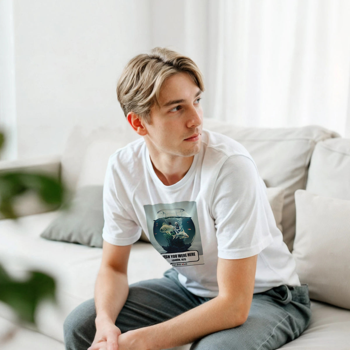 Ragazzo biondo seduto su un divano bianco, piegato in avanti, indossa la t-shirt bianca con la stampa Rock Art «Wish You Were Here – London, 1975»