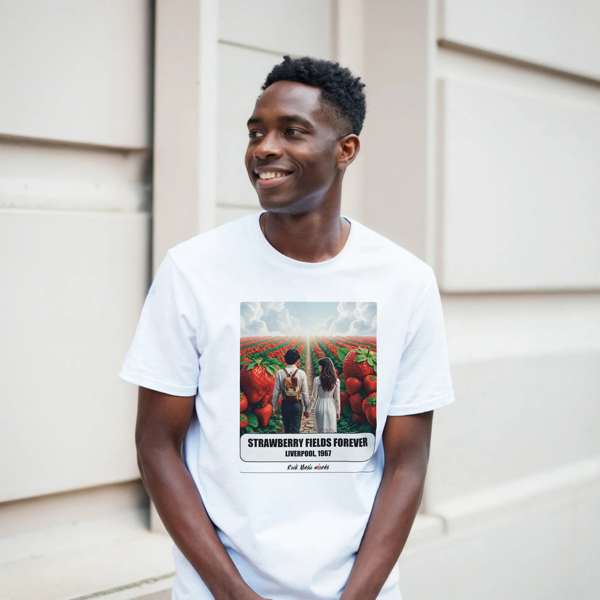 Ragazzo sorridente davanti a un muro chiaro a blocchi indossa la t-shirt bianca con la stampa Rock Art «Strawberry Fields Forever – Liverpool, 1967»