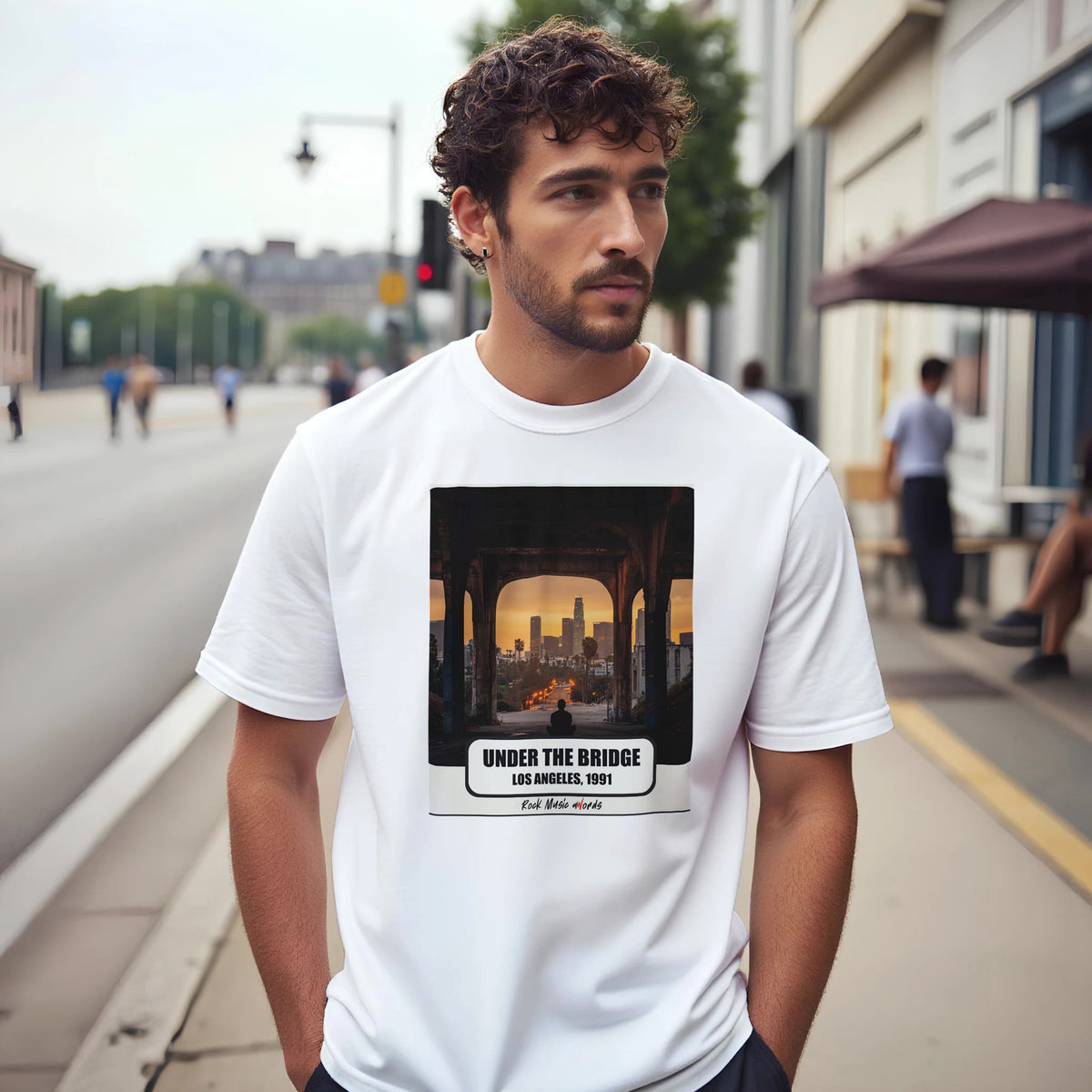 Uomo con capelli ricci e barba su un marciapiede di città indossa la t-shirt bianca con la stampa Rock Art «Under the Bridge – Los Angeles, 1991»