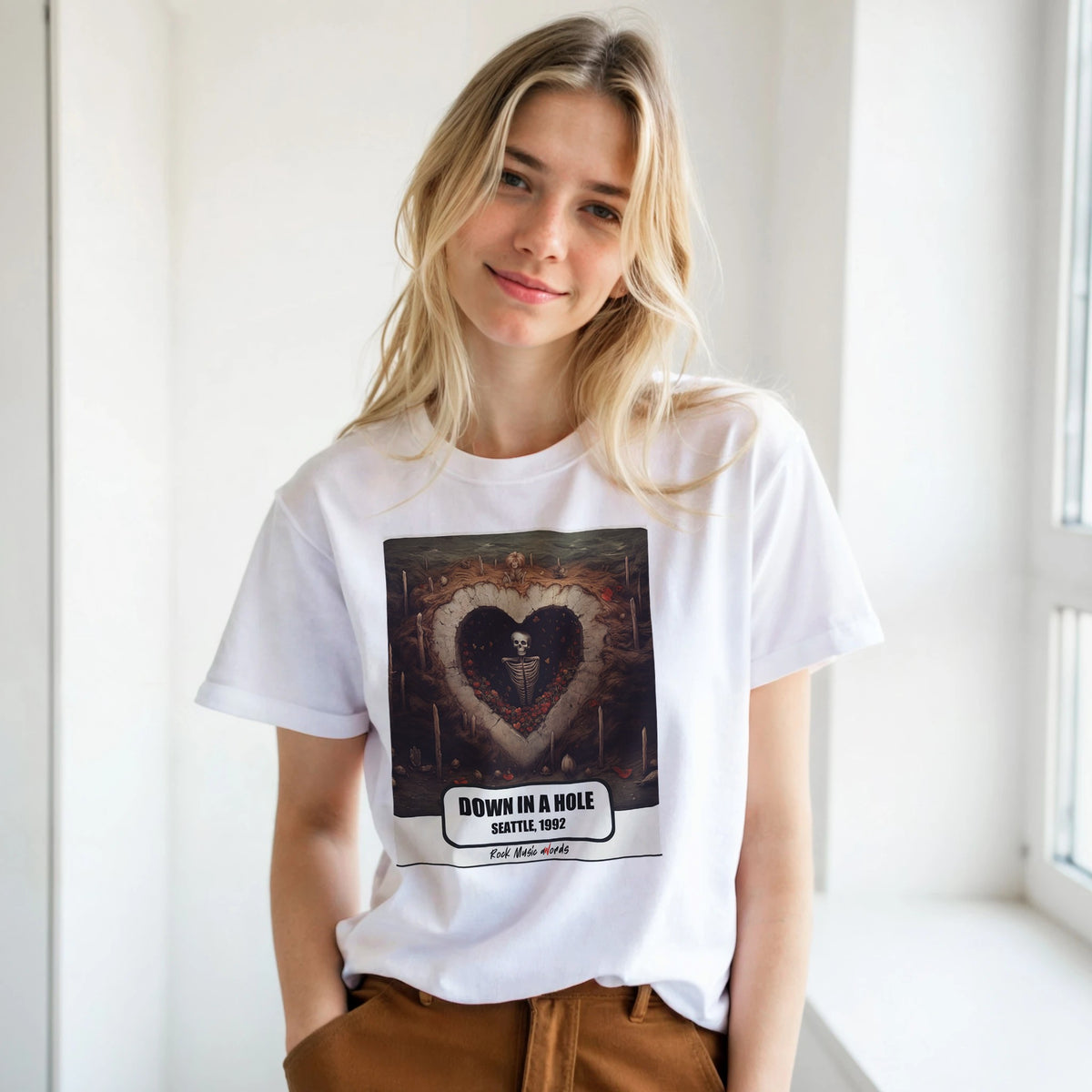 Ragazza bionda con le mani in tasca, accanto a una finestra, indossa la t-shirt bianca con la stampa Rock Art «Down in a Hole – Seattle, 1992»