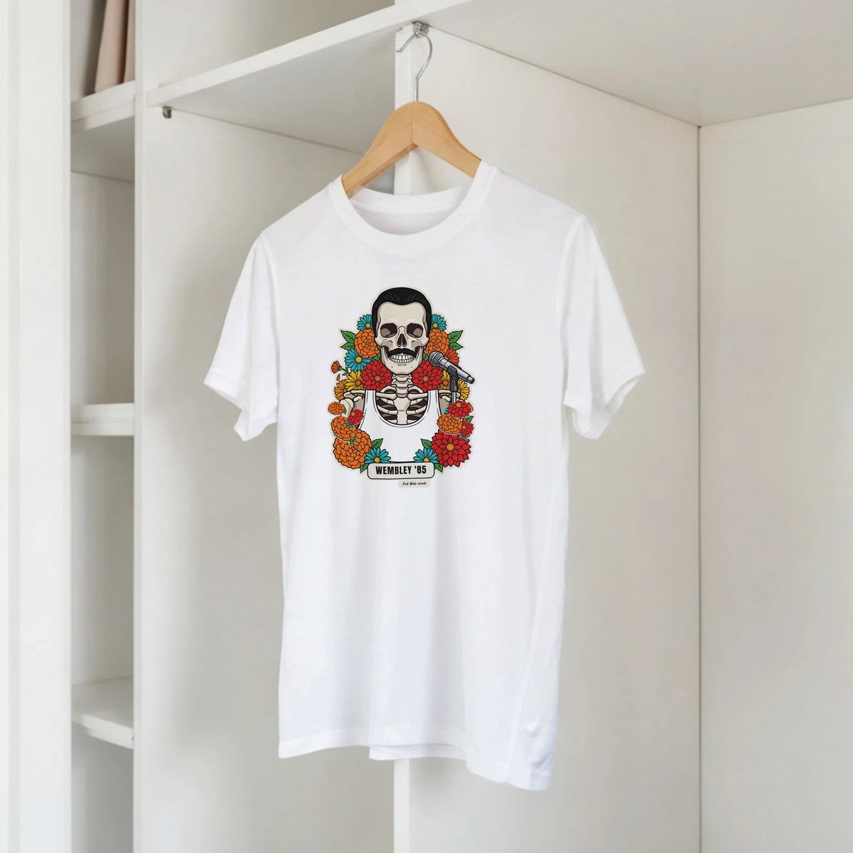 T-shirt bianca con la calavera Wembley '85 su una gruccia di legno, appesa a una libreria bianca