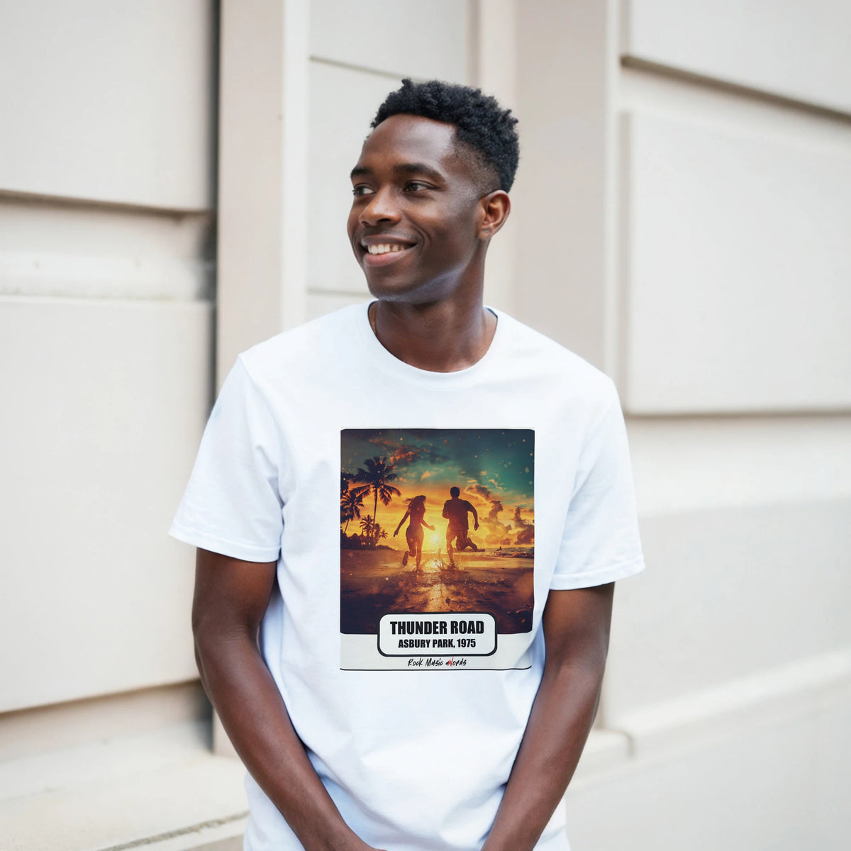 Ragazzo sorridente davanti a un muro chiaro a blocchi indossa la t-shirt bianca con la stampa Rock Art «Thunder Road – Asbury Park, 1975»