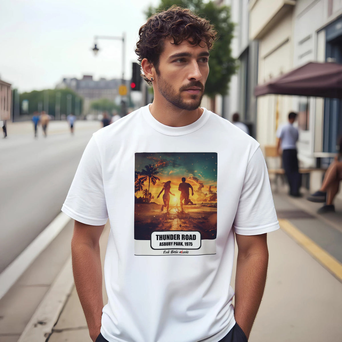 Uomo con capelli ricci e barba su un marciapiede di città indossa la t-shirt bianca con la stampa Rock Art «Thunder Road – Asbury Park, 1975»