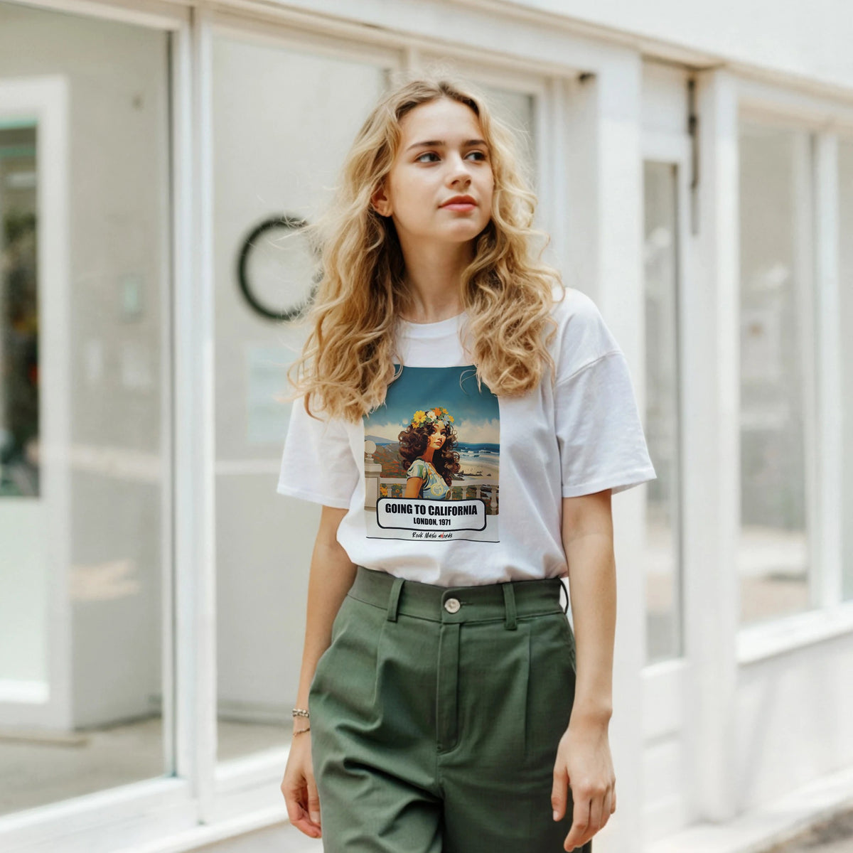 Ragazza bionda davanti a una facciata a vetrate indossa la t-shirt bianca con la stampa Rock Art «Going to California – London, 1971» e pantaloni verdi