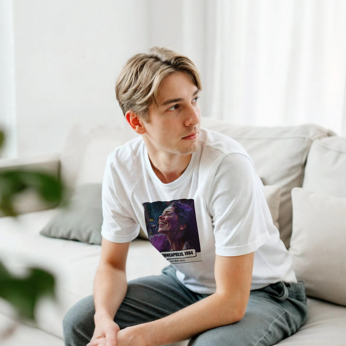 Ragazzo biondo seduto su un divano bianco, piegato in avanti, indossa la t-shirt bianca con la stampa Rock Art «Purple Rain – Minneapolis, 1984»