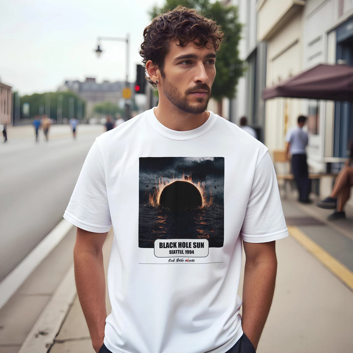 Uomo con capelli ricci e barba su un marciapiede di città indossa la t-shirt bianca con la stampa Rock Art «Black Hole Sun – Seattle, 1994»
