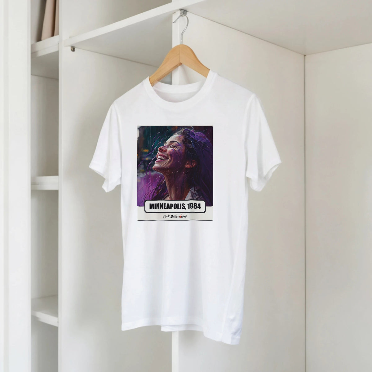 T-shirt bianca con la stampa Rock Art «Purple Rain – Minneapolis, 1984» su una gruccia di legno, appesa a una libreria bianca
