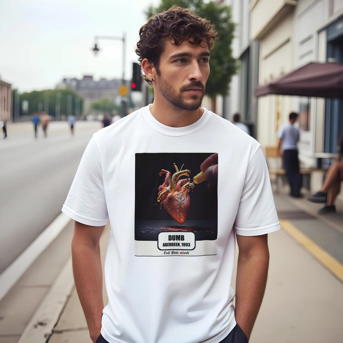 Uomo con capelli ricci e barba su un marciapiede di città indossa la t-shirt bianca con la stampa Rock Art «Dumb – Aberdeen, 1993»