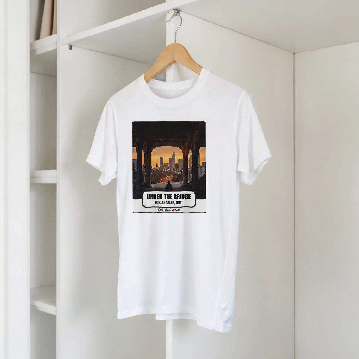 T-shirt bianca con la stampa Rock Art «Under the Bridge – Los Angeles, 1991» su una gruccia di legno, appesa a una libreria bianca