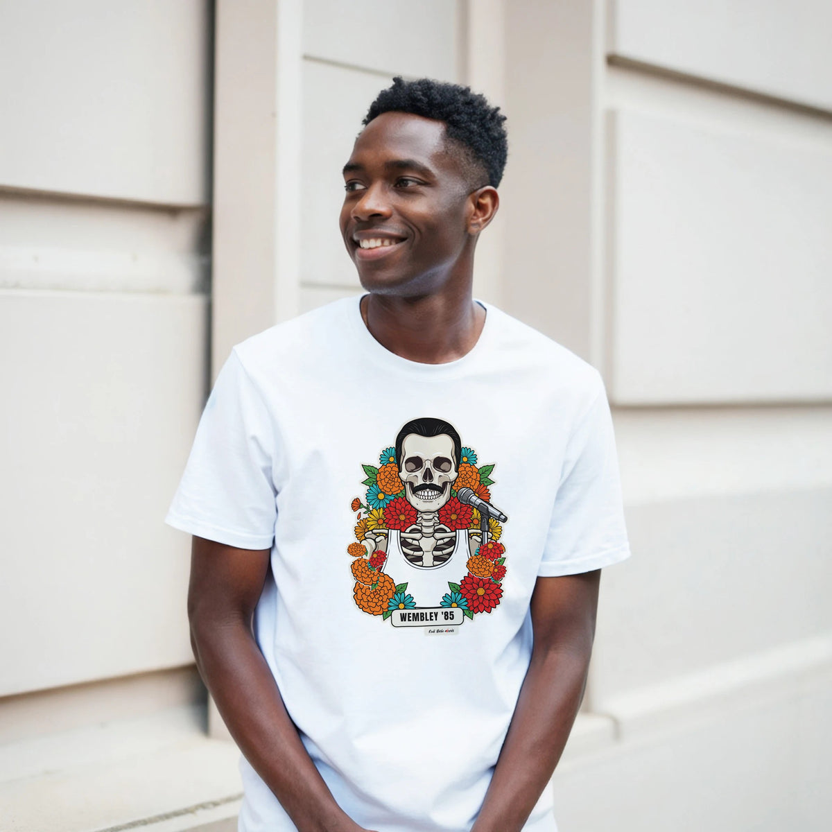Ragazzo sorridente davanti a un muro chiaro a blocchi indossa la t-shirt bianca con la calavera Wembley '85