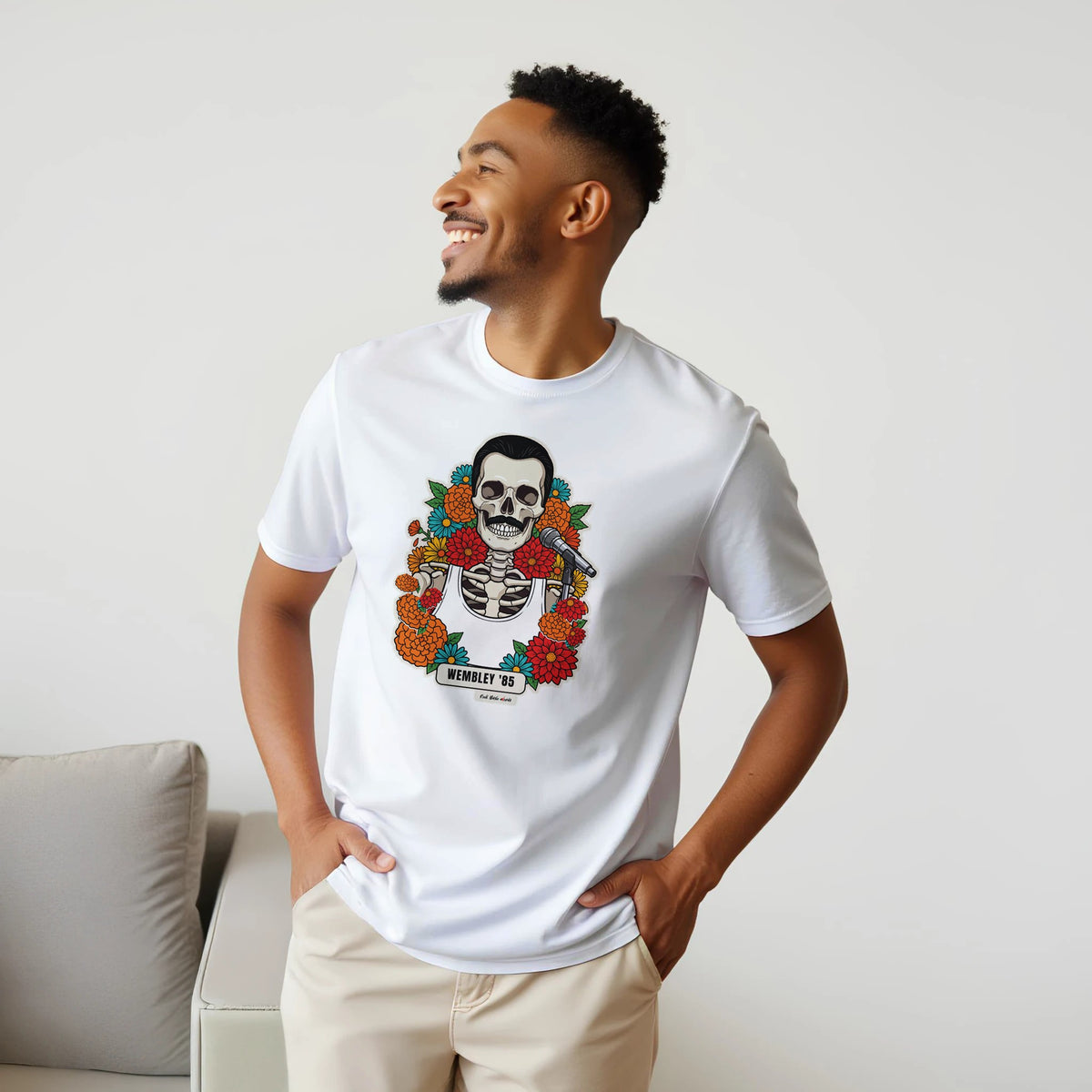 Uomo sorridente con le mani sui fianchi, accanto a un divano, indossa la t-shirt bianca con la calavera Wembley '85
