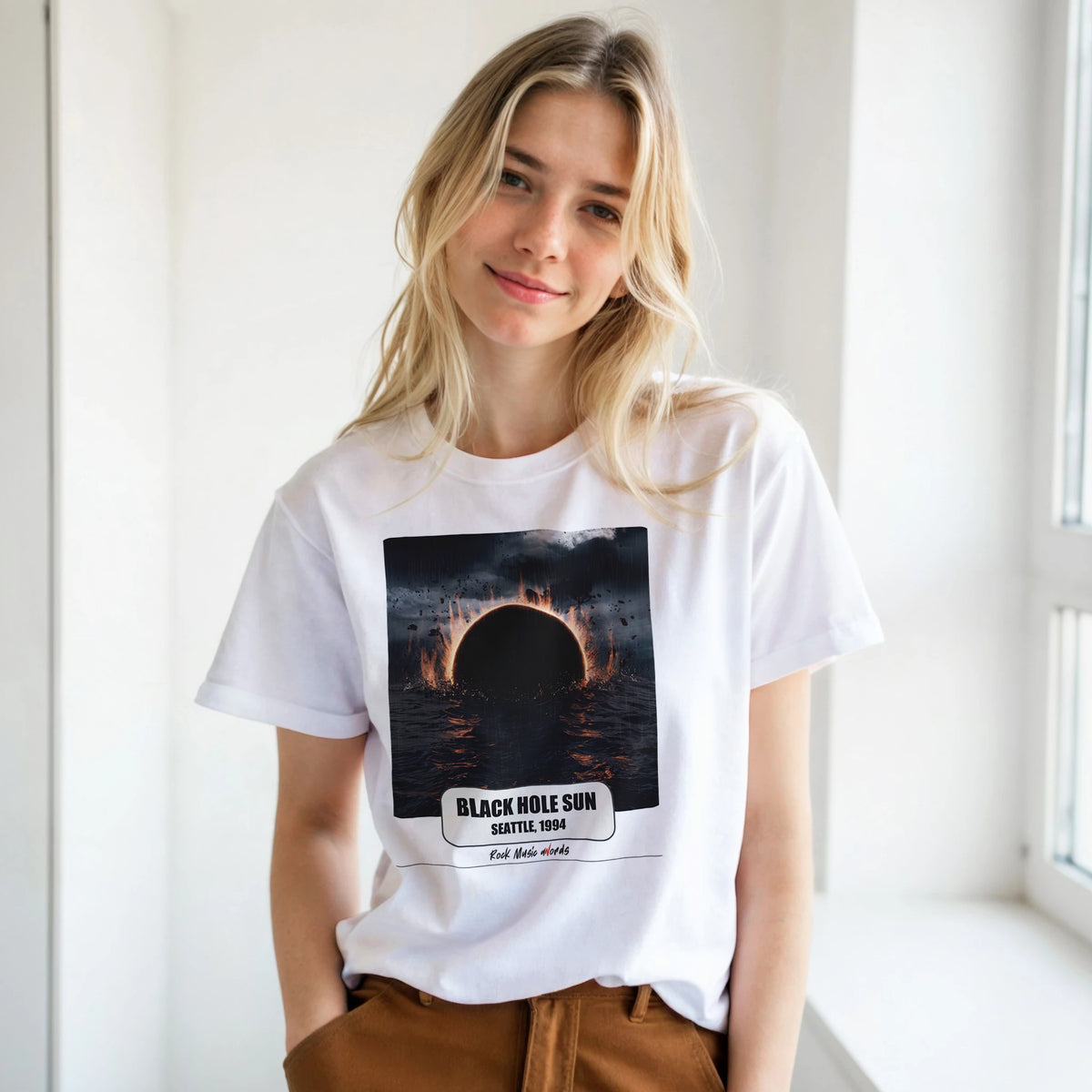 Ragazza bionda con le mani in tasca, accanto a una finestra, indossa la t-shirt bianca con la stampa Rock Art «Black Hole Sun – Seattle, 1994»