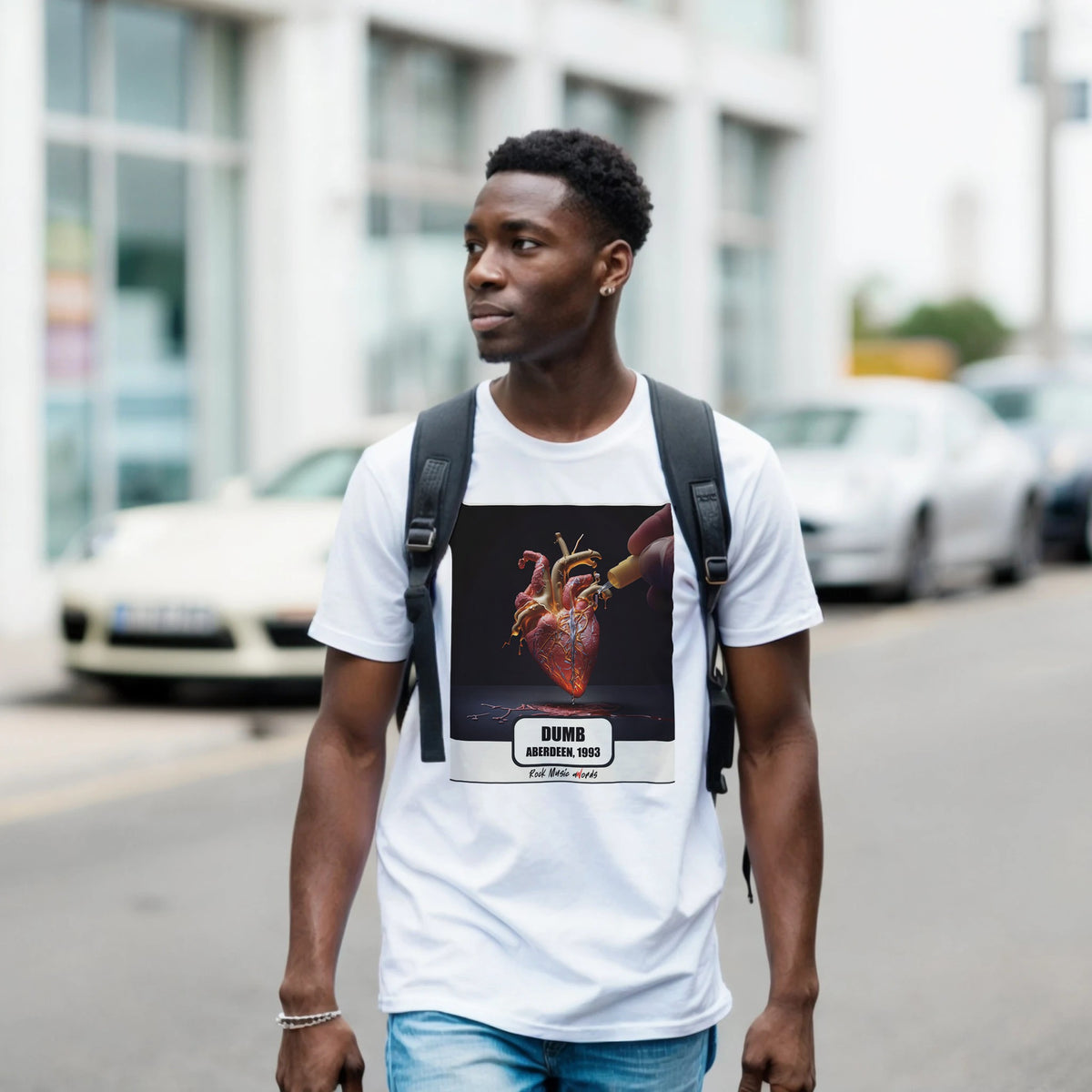 Ragazzo con zaino nero e jeans cammina per una via di città indossando la t-shirt bianca con la stampa Rock Art «Dumb – Aberdeen, 1993»