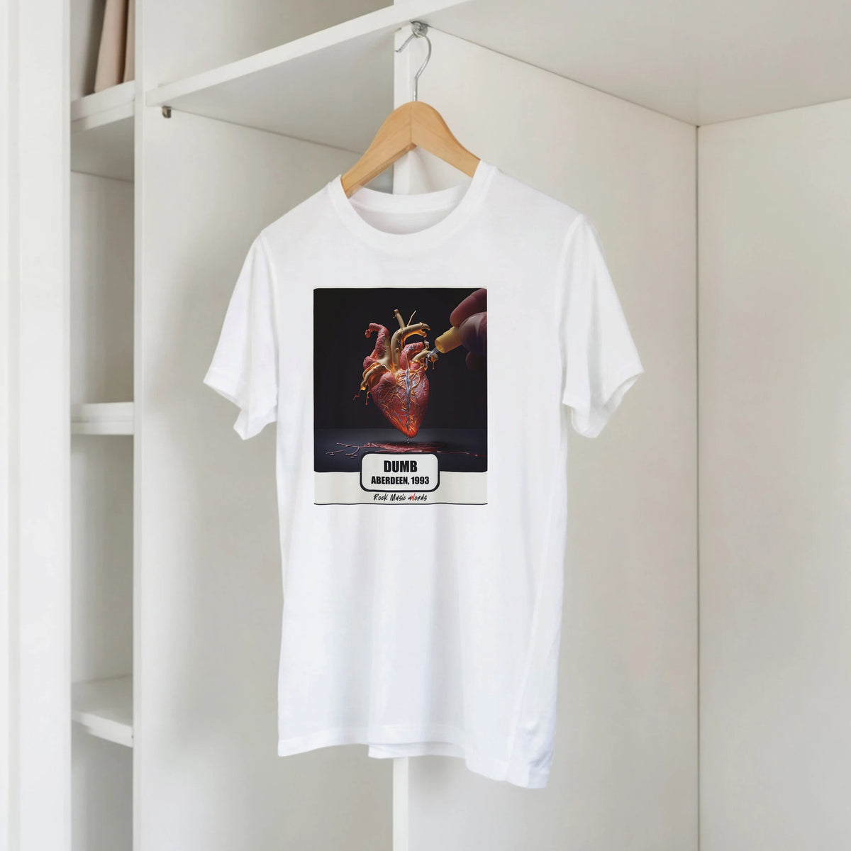T-shirt bianca con la stampa Rock Art «Dumb – Aberdeen, 1993» su una gruccia di legno, appesa a una libreria bianca