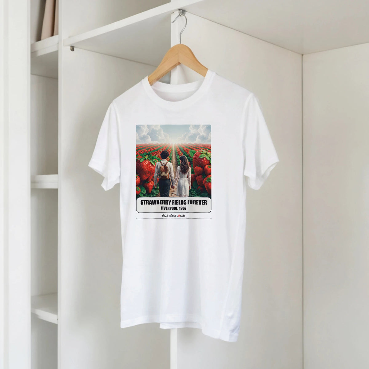 T-shirt bianca con la stampa Rock Art «Strawberry Fields Forever – Liverpool, 1967» su una gruccia di legno, appesa a una libreria bianca