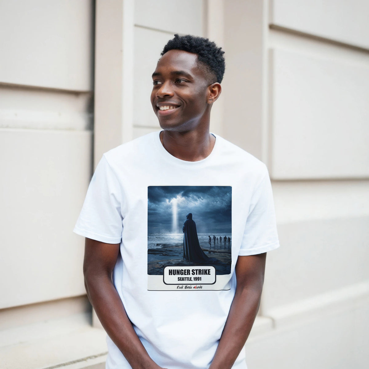 Ragazzo sorridente davanti a un muro chiaro a blocchi indossa la t-shirt bianca con la stampa Rock Art «Hunger Strike – Seattle, 1991»