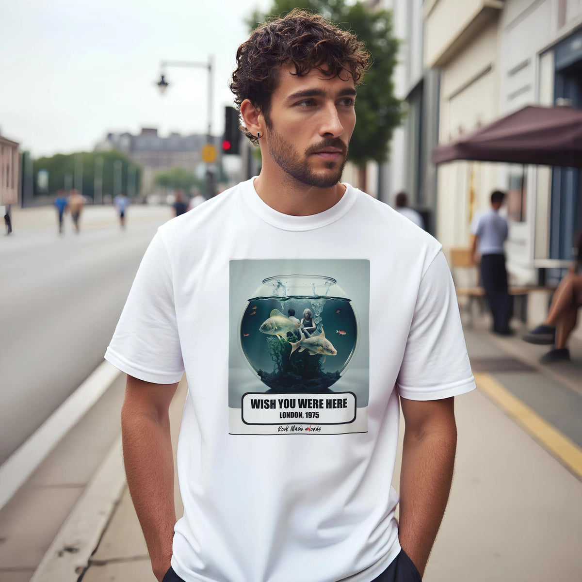 Uomo con capelli ricci e barba su un marciapiede di città indossa la t-shirt bianca con la stampa Rock Art «Wish You Were Here – London, 1975»