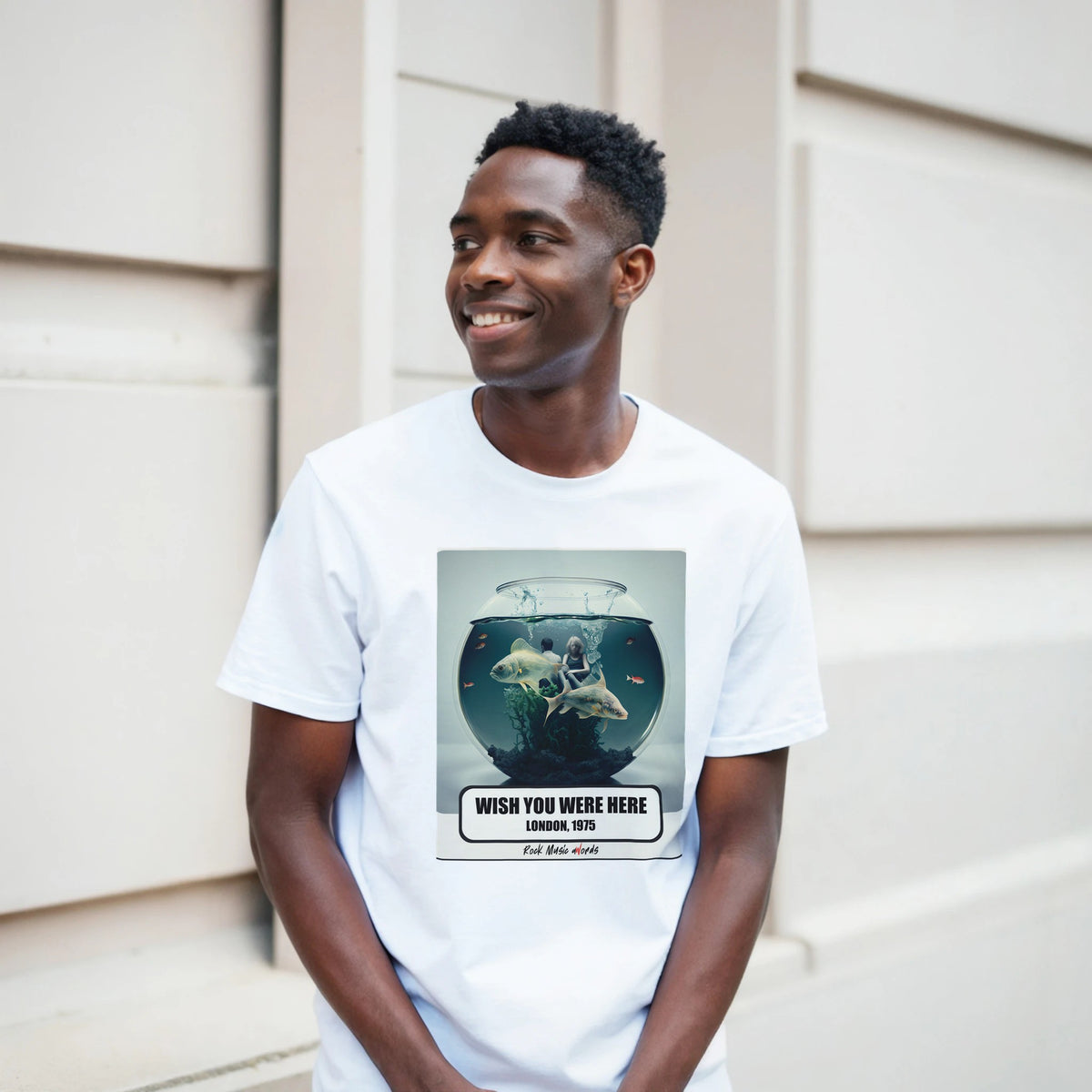 Ragazzo sorridente davanti a un muro chiaro a blocchi indossa la t-shirt bianca con la stampa Rock Art «Wish You Were Here – London, 1975»