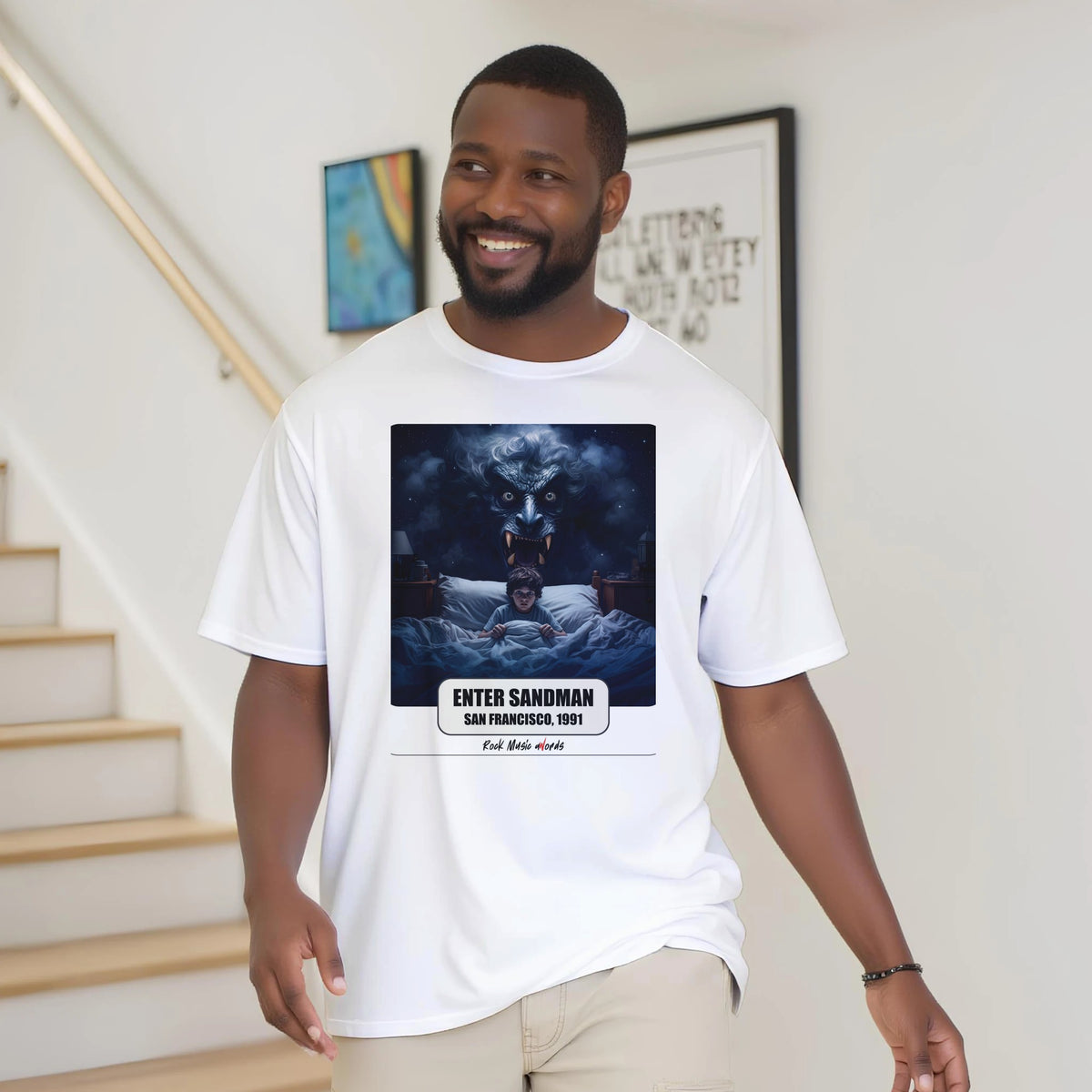 Uomo con la barba sorride vicino a una scala di legno, in casa, e indossa la t-shirt bianca con la stampa Rock Art «Enter Sandman – San Francisco, 1991»