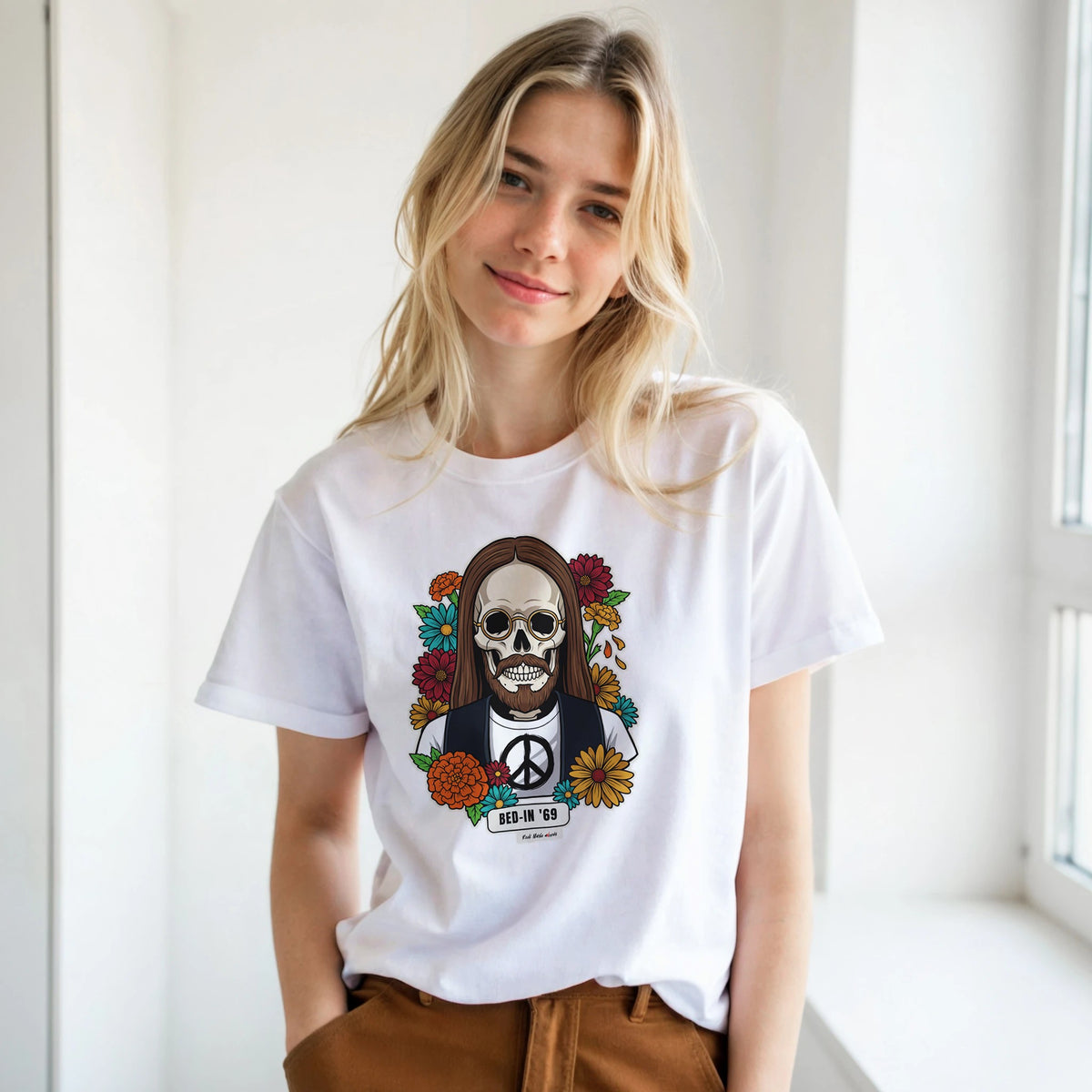 Ragazza bionda con le mani in tasca, accanto a una finestra, indossa la t-shirt bianca con la calavera Bed-In '69