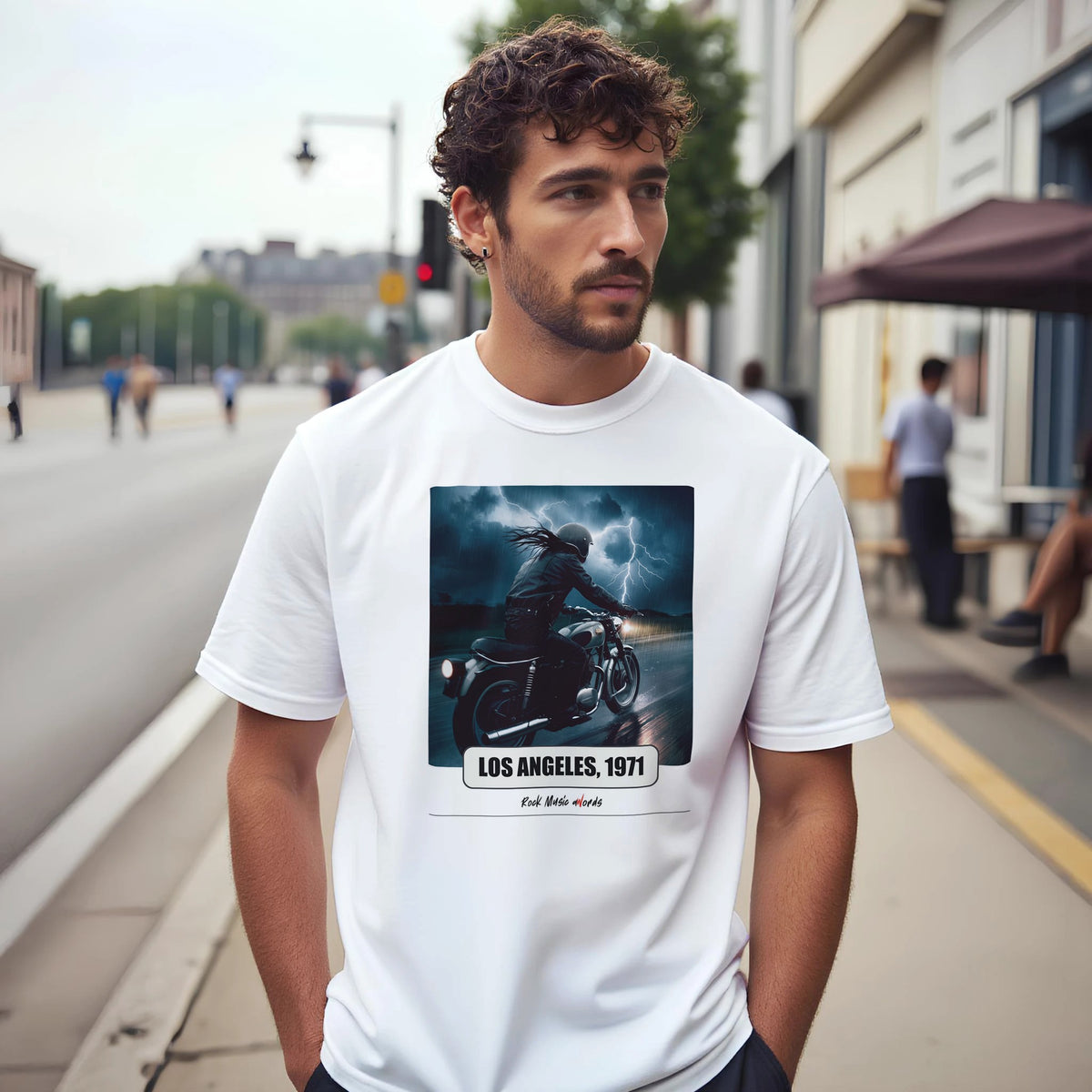 Uomo con capelli ricci e barba su un marciapiede di città indossa la t-shirt bianca con la stampa Rock Art «Riders on the Storm – Los Angeles, 1971»