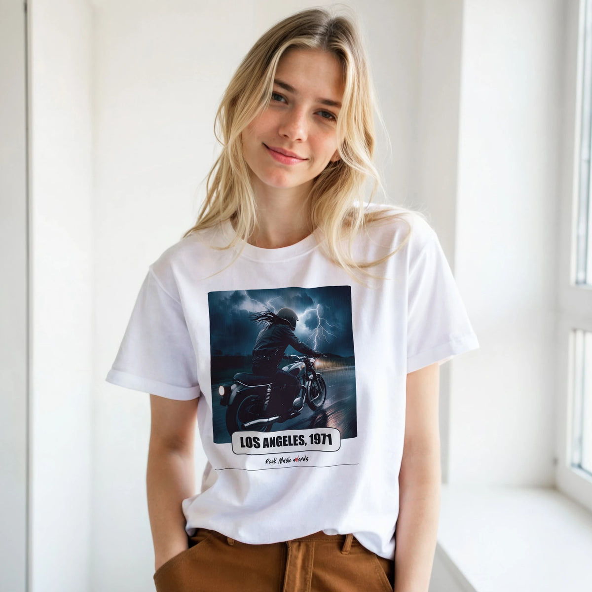 Ragazza bionda con le mani in tasca, accanto a una finestra, indossa la t-shirt bianca con la stampa Rock Art «Riders on the Storm – Los Angeles, 1971»