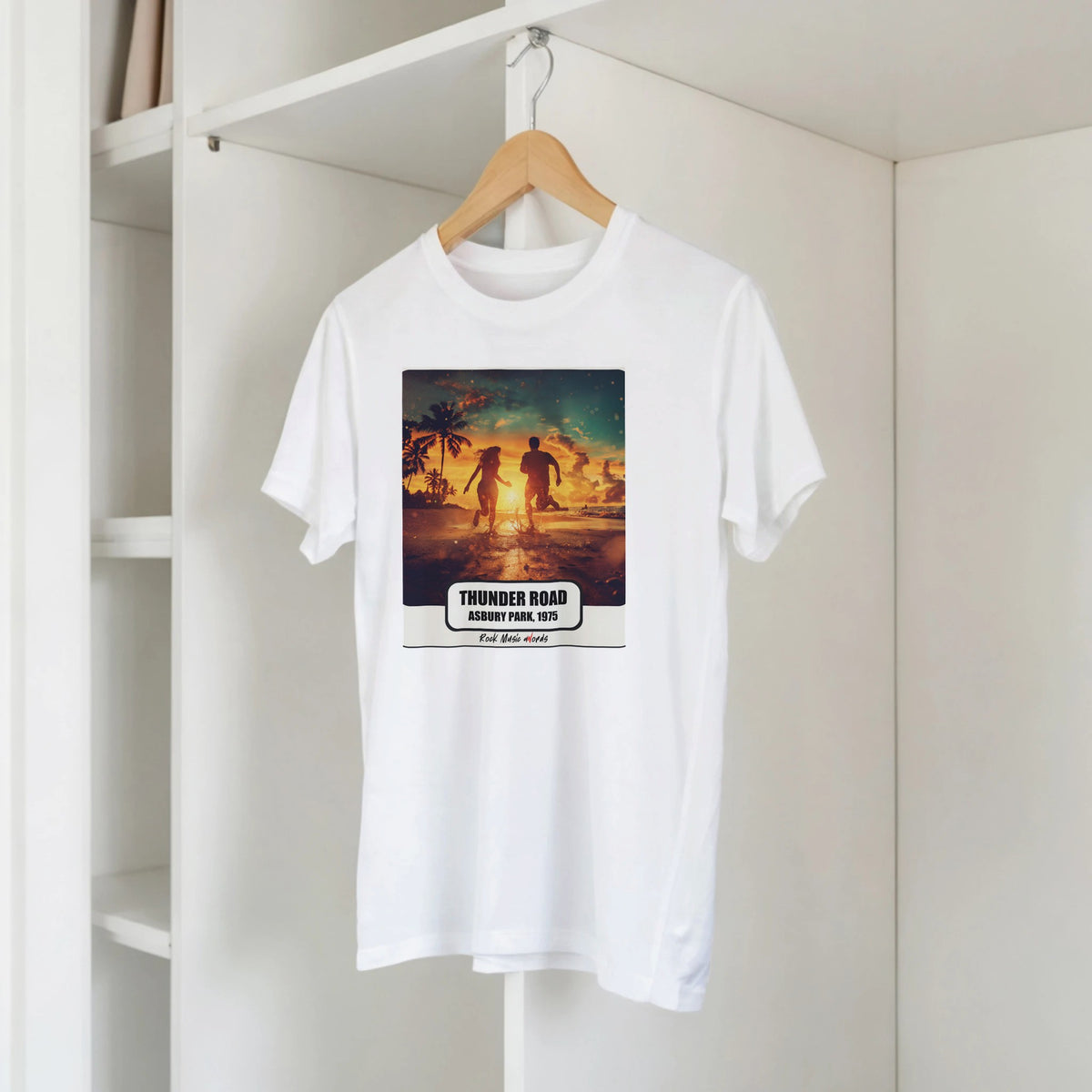 T-shirt bianca con la stampa Rock Art «Thunder Road – Asbury Park, 1975» su una gruccia di legno, appesa a una libreria bianca