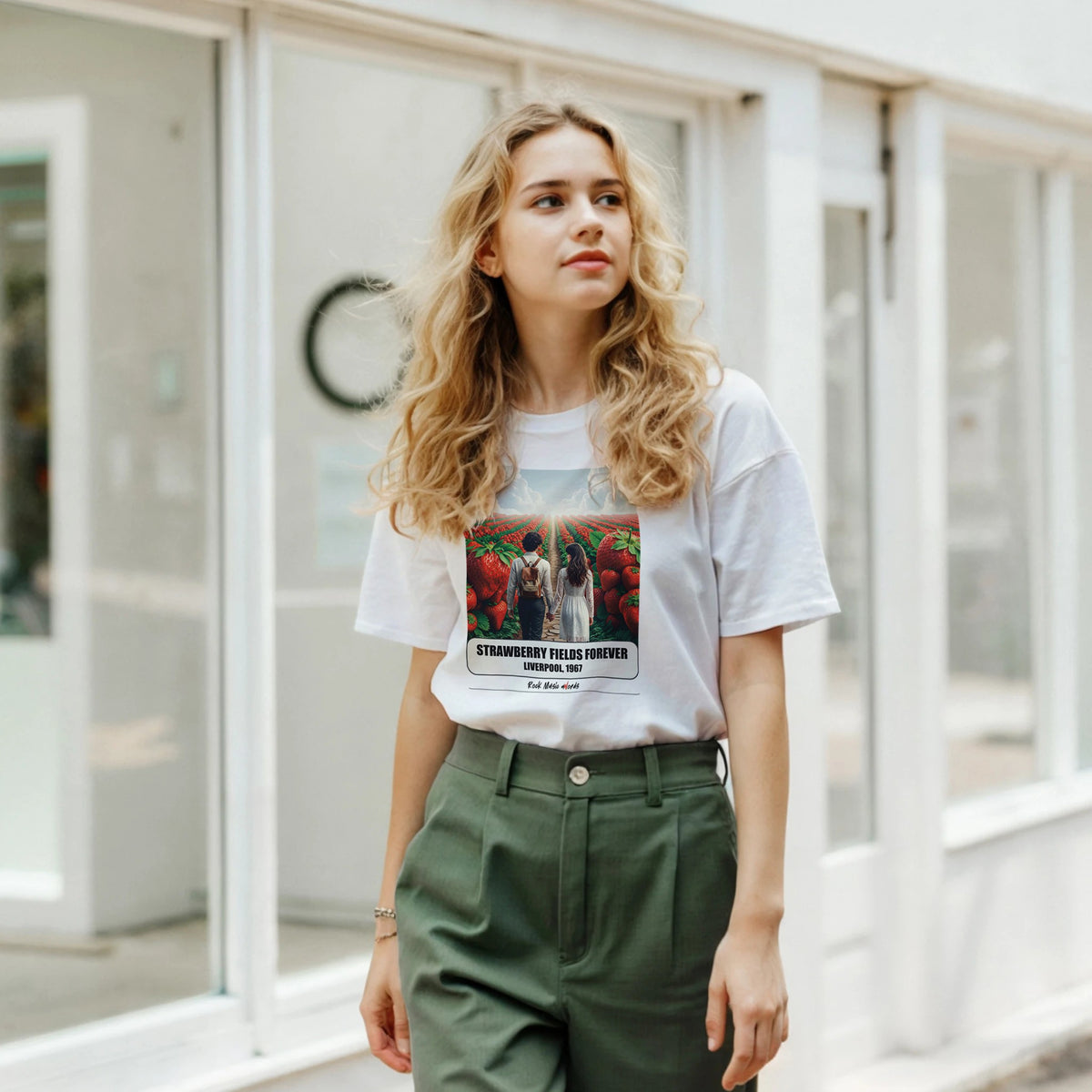 Ragazza bionda davanti a una facciata a vetrate indossa la t-shirt bianca con la stampa Rock Art «Strawberry Fields Forever – Liverpool, 1967» e pantaloni verdi