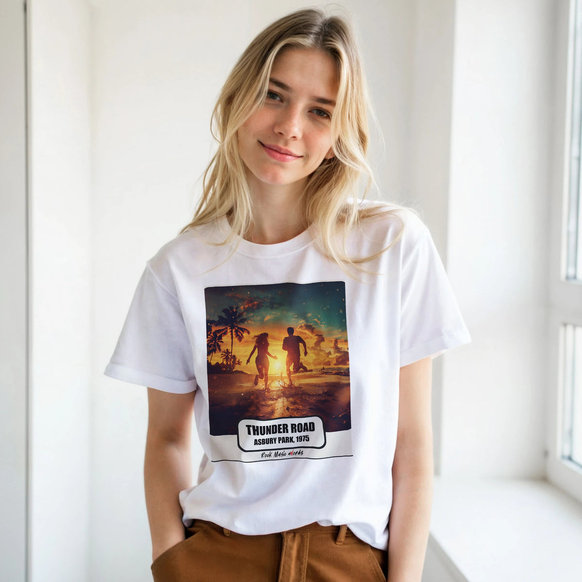 Ragazza bionda con le mani in tasca, accanto a una finestra, indossa la t-shirt bianca con la stampa Rock Art «Thunder Road – Asbury Park, 1975»
